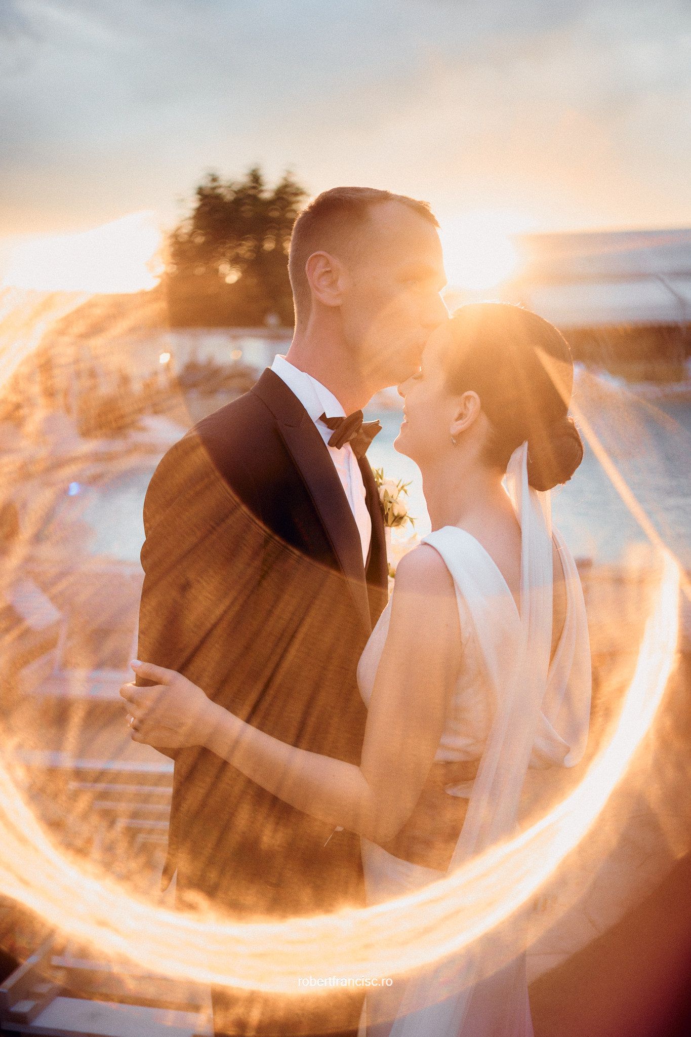 A glowing light trail circles around a couple in wedding attire at sunset creating a magical romantic effect.