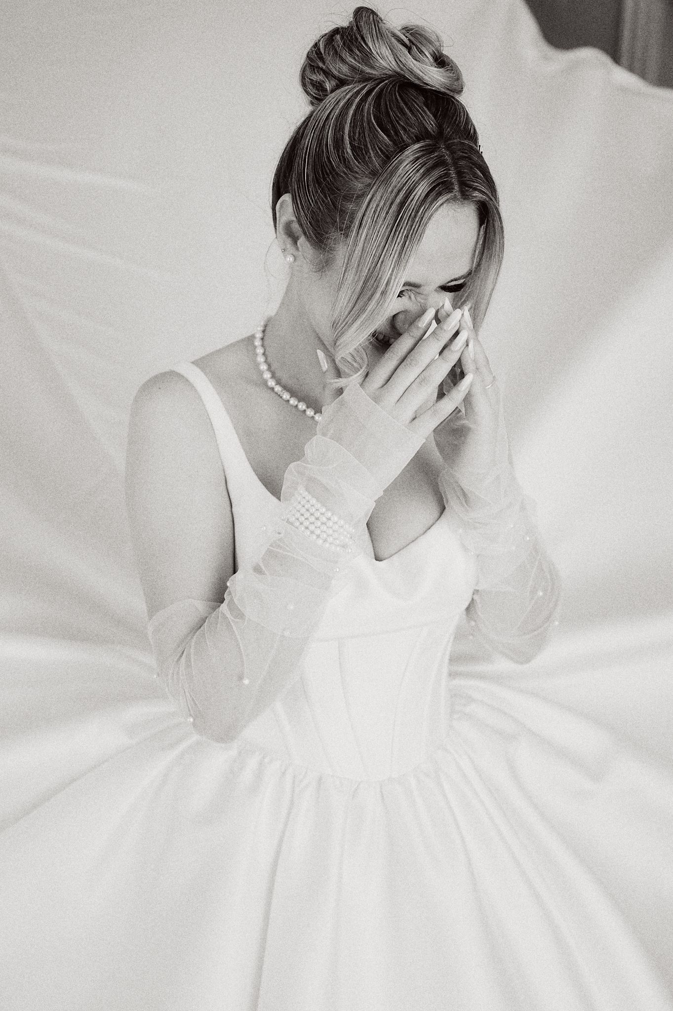 Black and white portrait of person in wedding dress covering face with gloved hand.
