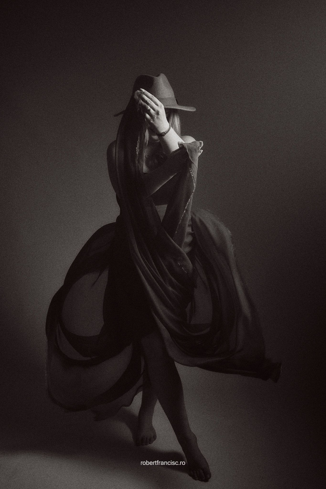 Dramatic black and white portrait of a dancer in flowing fabric making graceful movements against dark background.