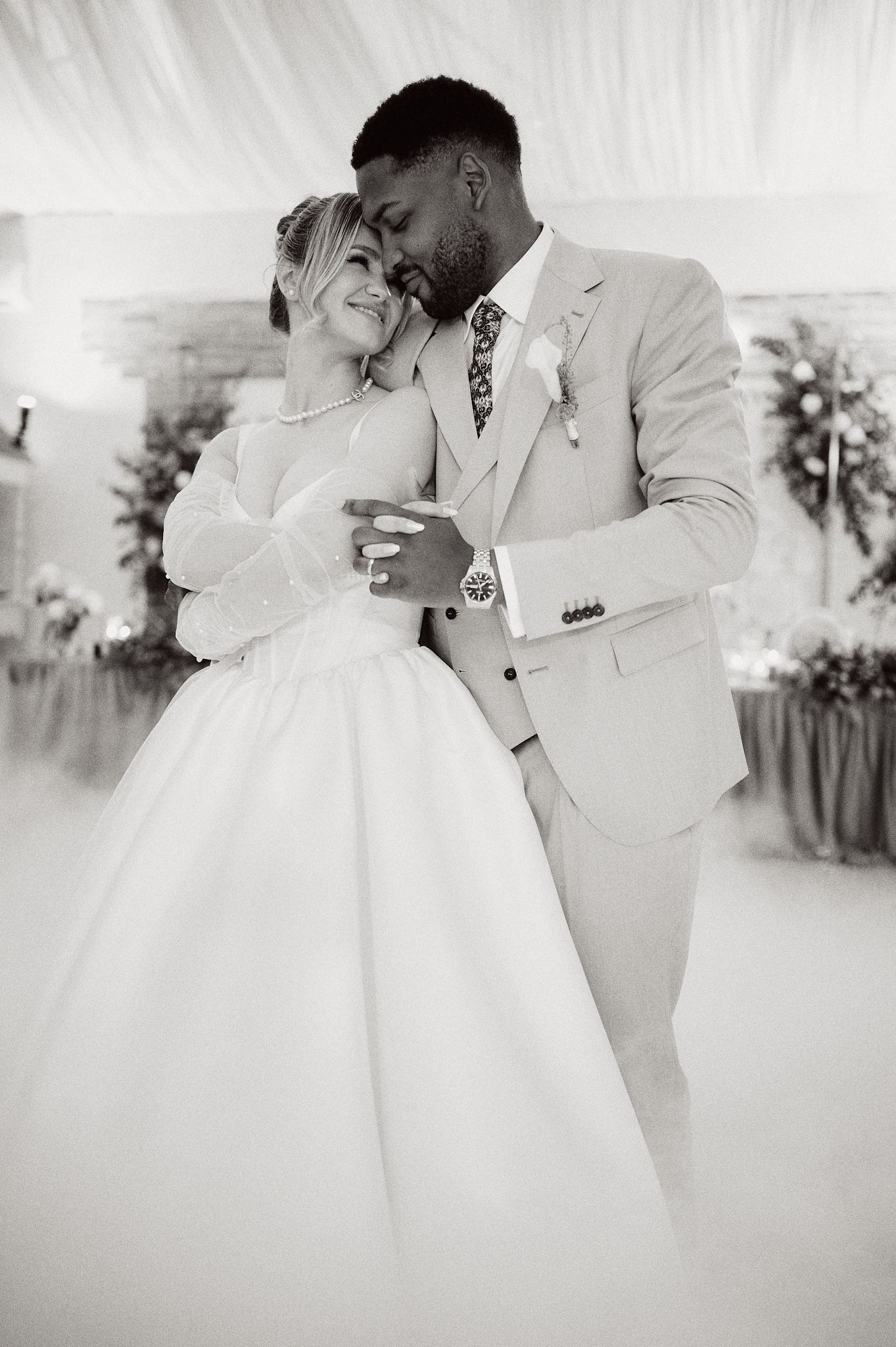 Romantic black and white portrait of newlyweds embracing under draped fabric.