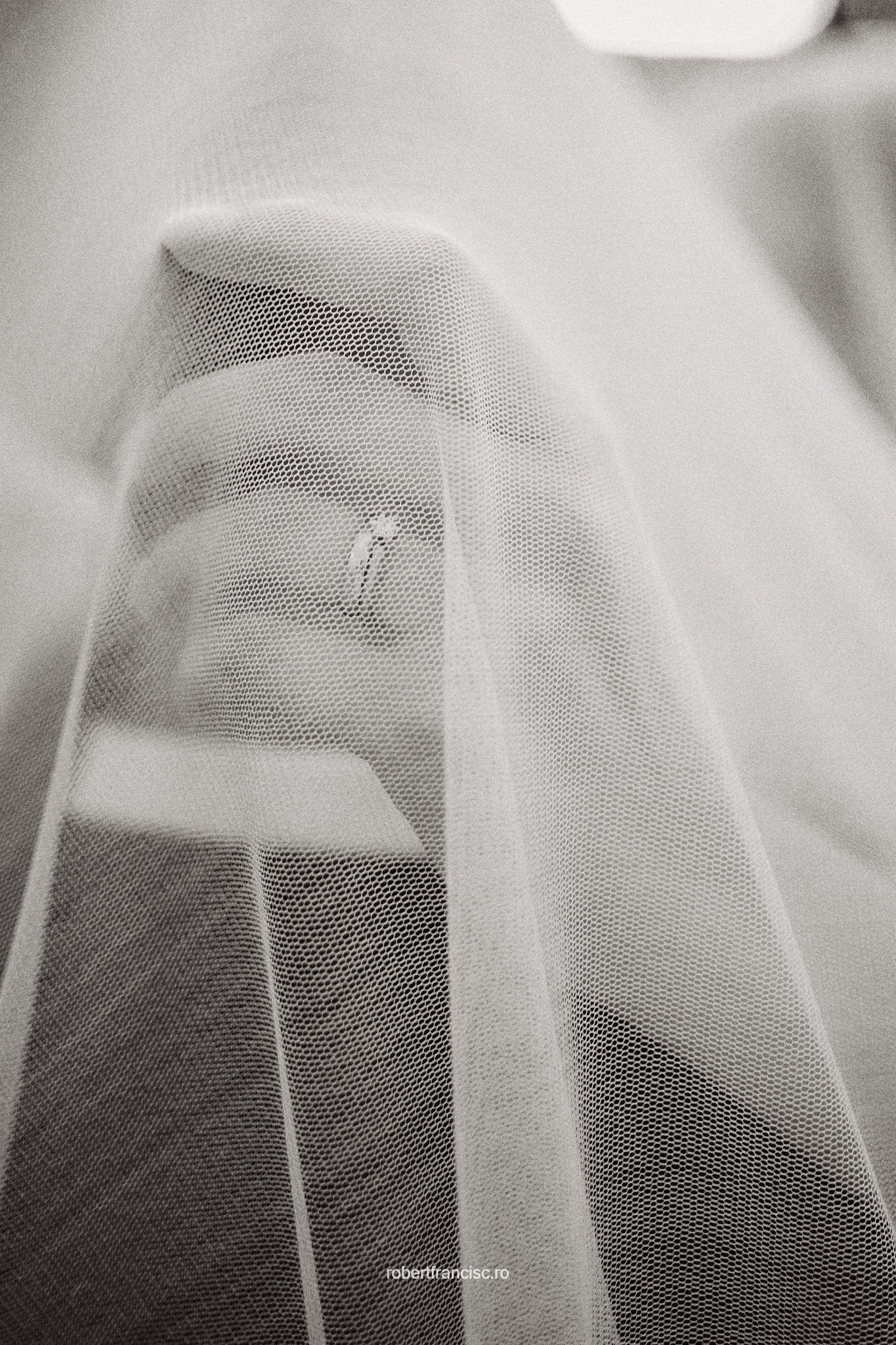 A diamond engagement ring sparkles through delicate layers of sheer white wedding veil fabric in black and white.