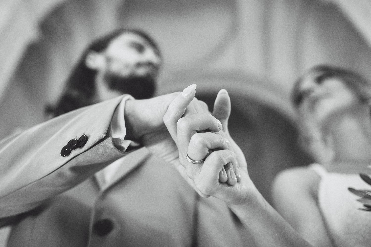 Black and white close-up of joined hands during wedding ceremony.