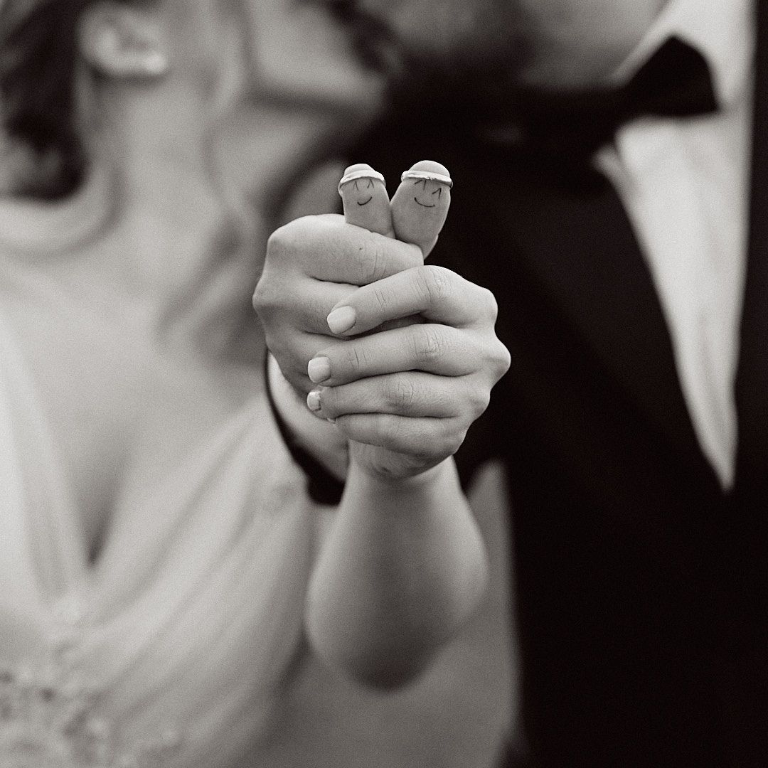 Black and white close-up of hands holding tiny decorative birds at wedding.