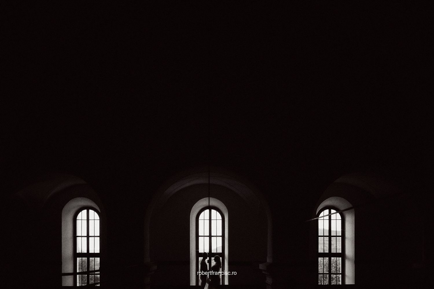 Gothic arched windows silhouetted against dark shadows create a dramatic architectural sequence at night.