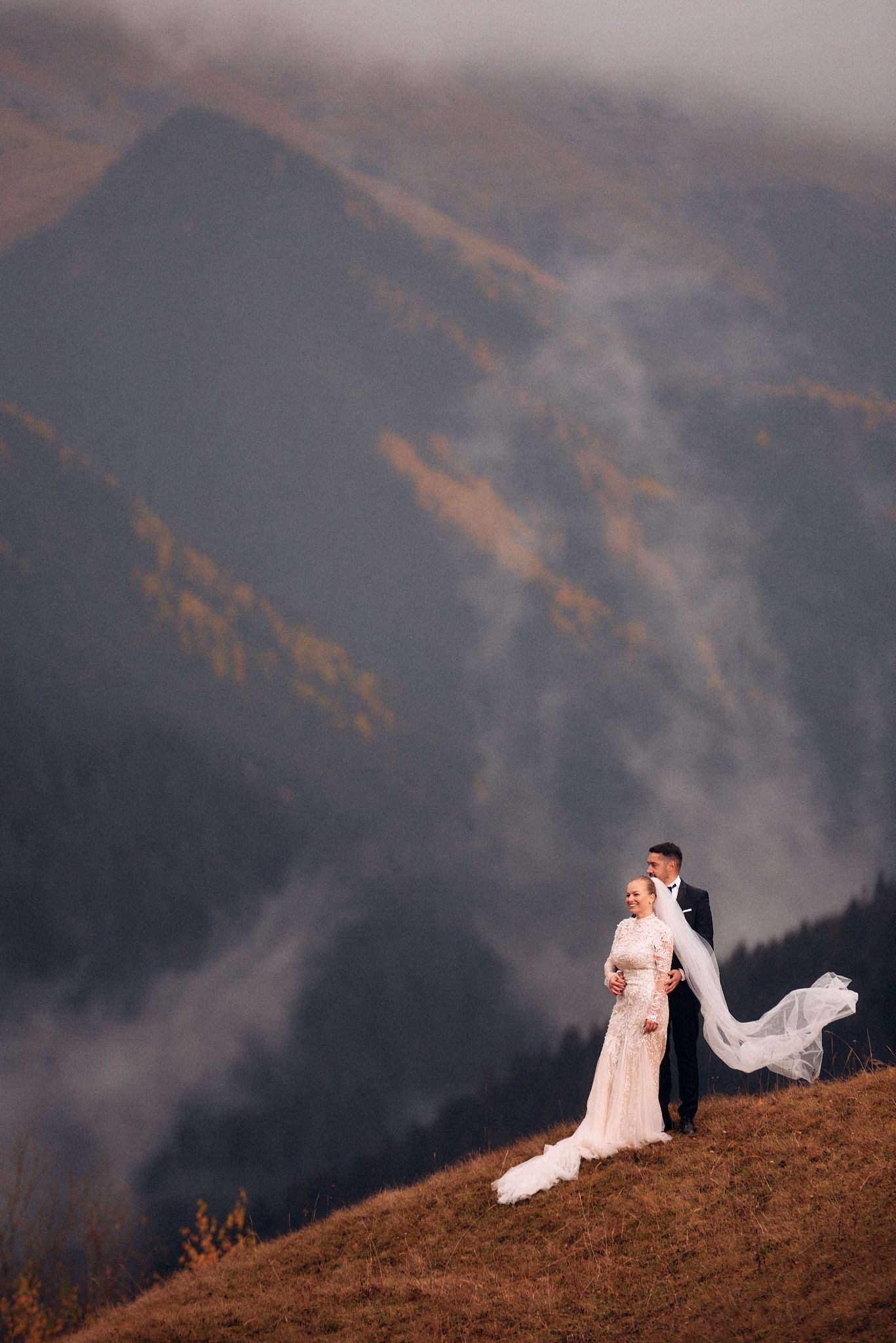 A dramatic mountain wedding portrait with swirling fog and autumn colors.