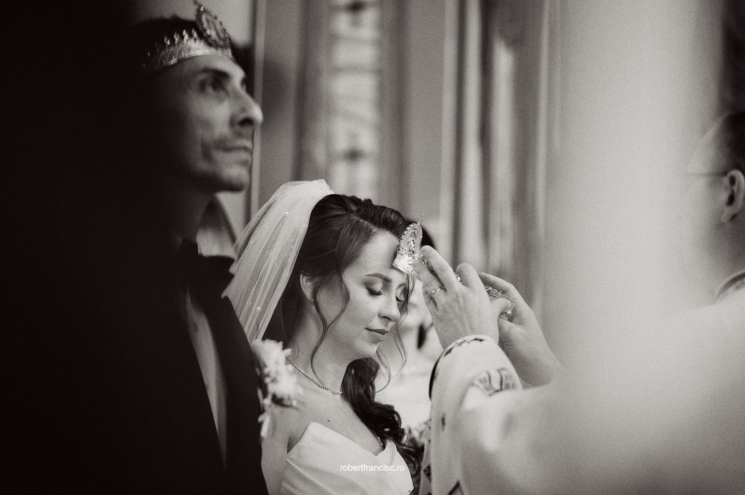 A black and white wedding photograph showing a bride having her veil adjusted in a soft, candid moment.
