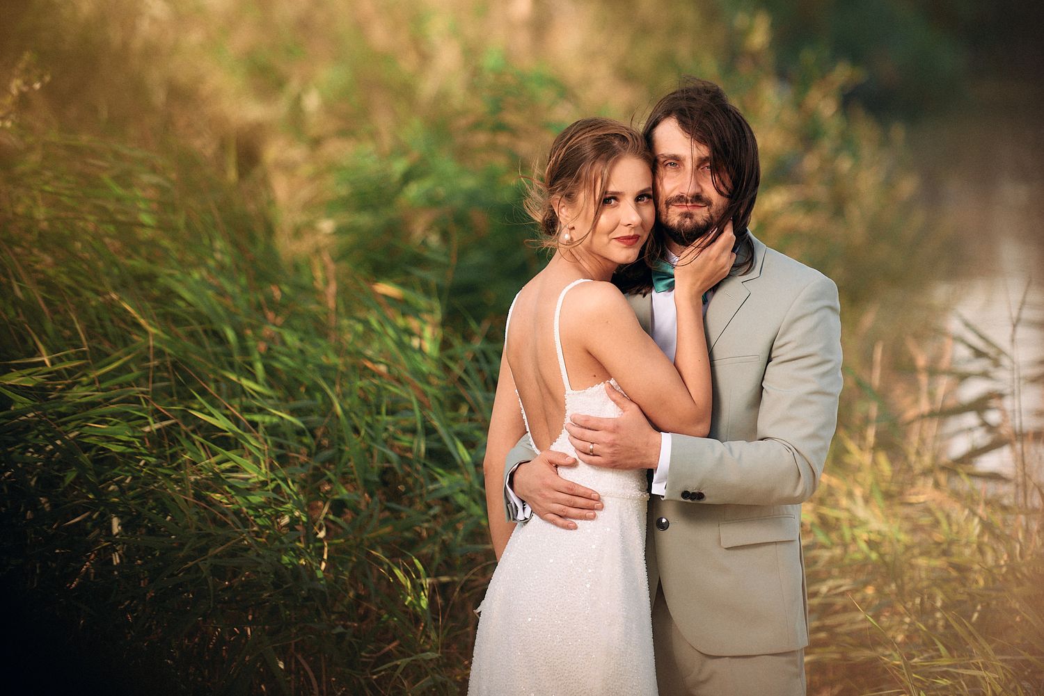 A romantic wedding portrait of a couple embracing in tall grass during golden hour.
