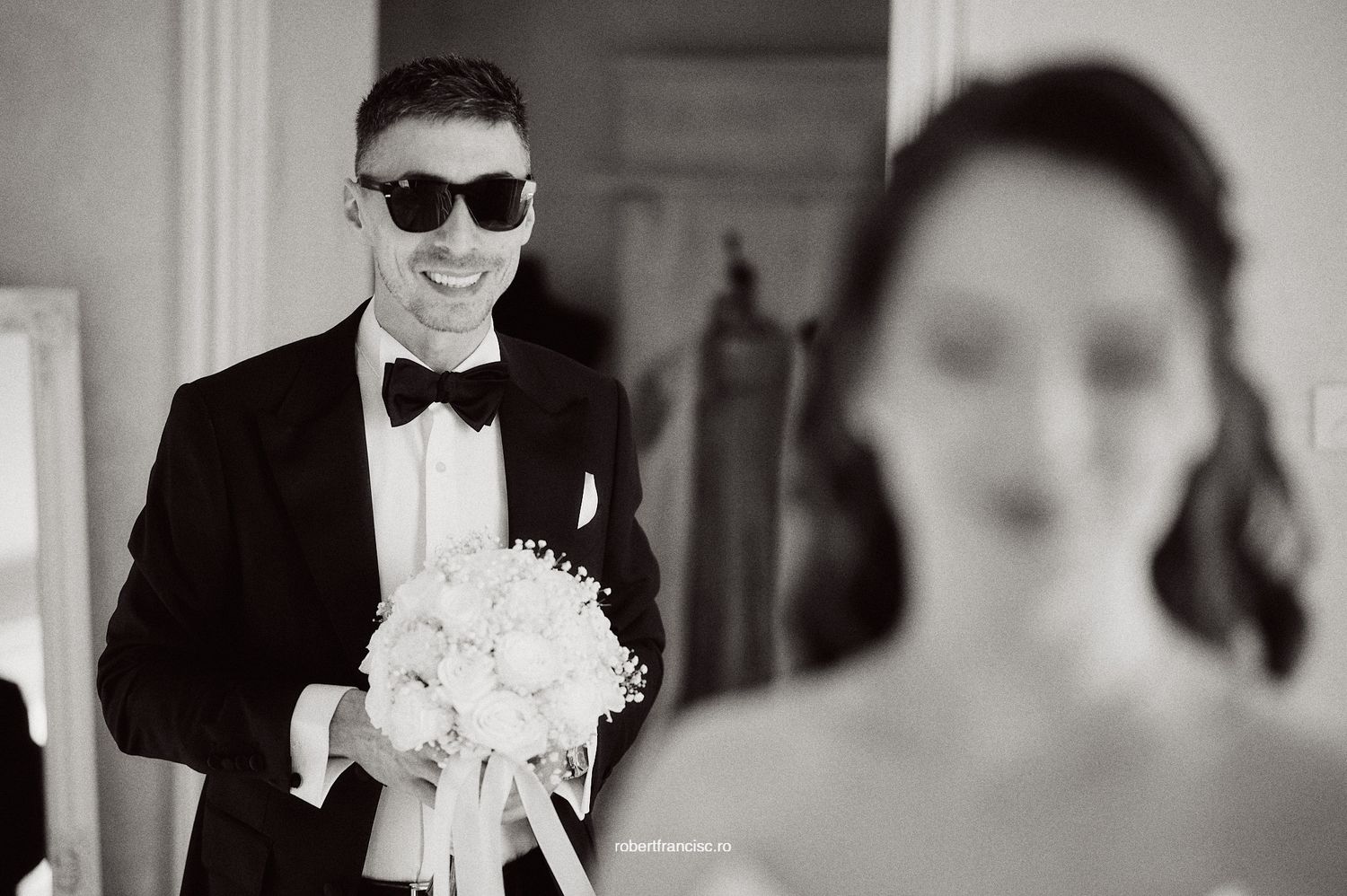 Black and white wedding photo showing elegant formal attire and white floral bouquet.