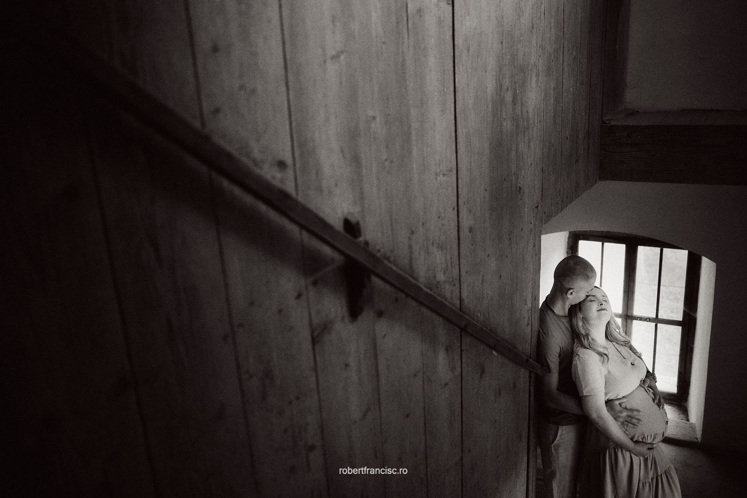 Window light illuminates interior of dark wooden attic space in grainy black and white photography.