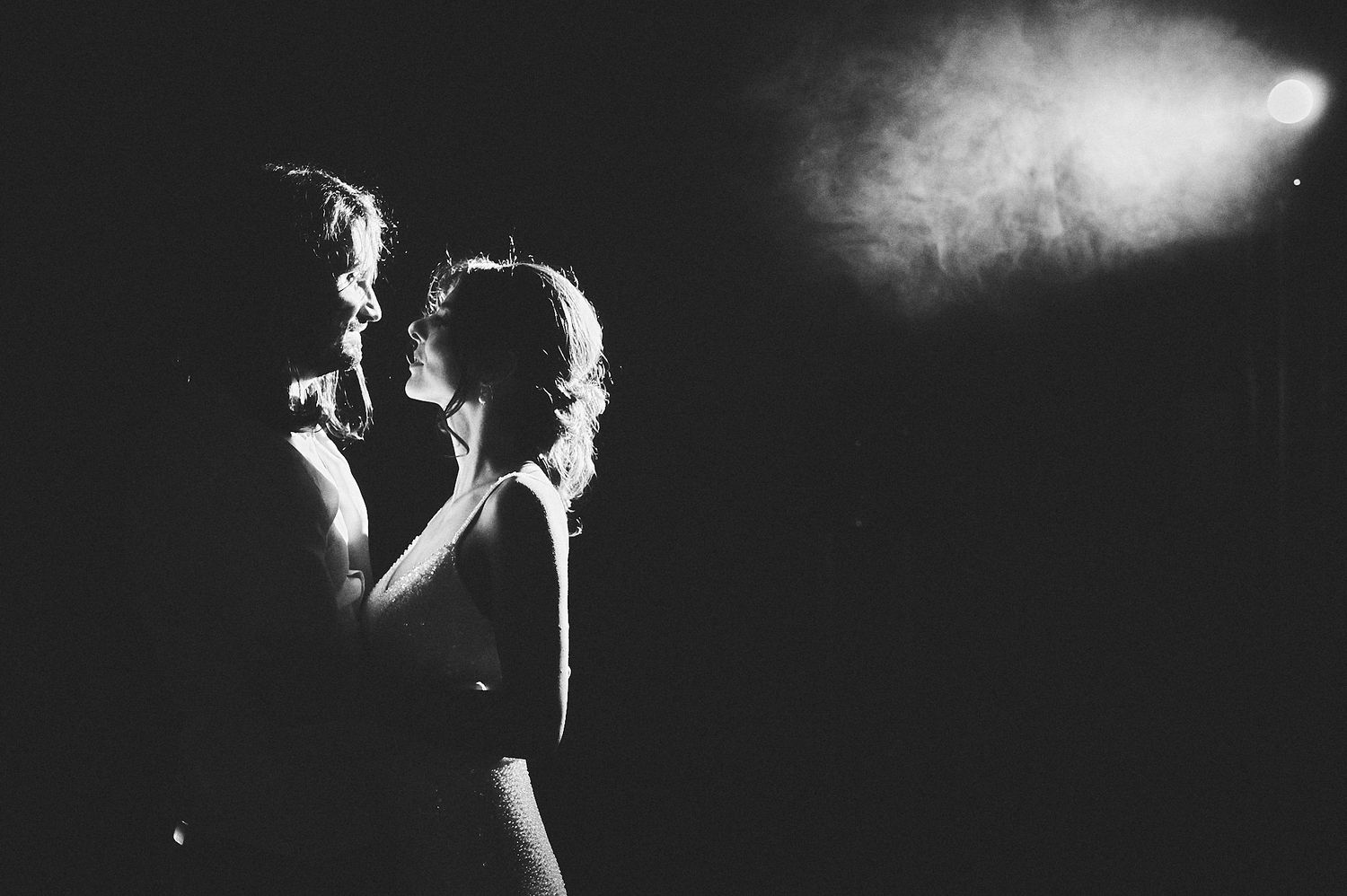 Silhouetted figures share a romantic dance moment against bright spotlight.