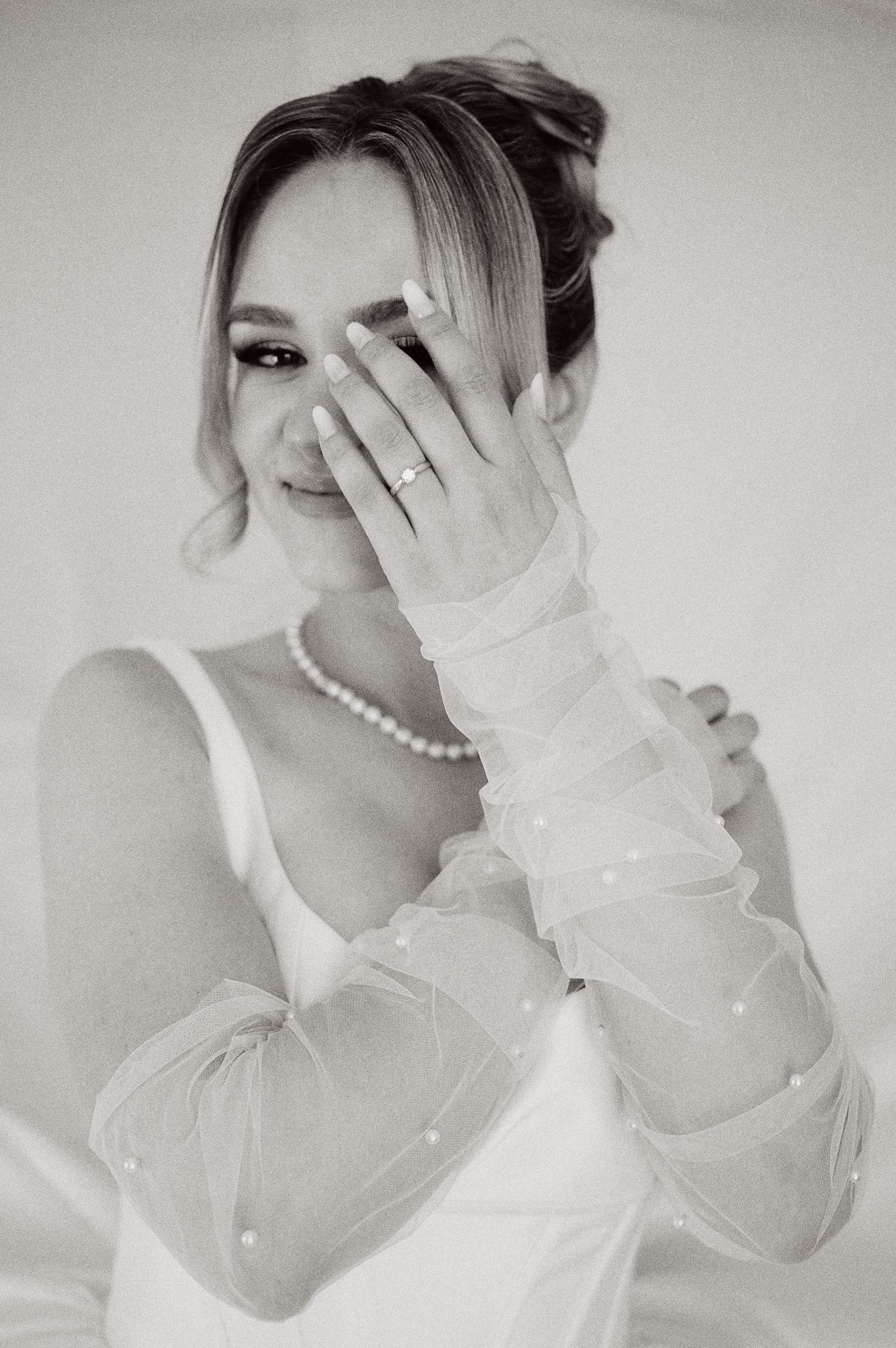Elegant bridal portrait with pearl necklace and sheer gloves in black and white.