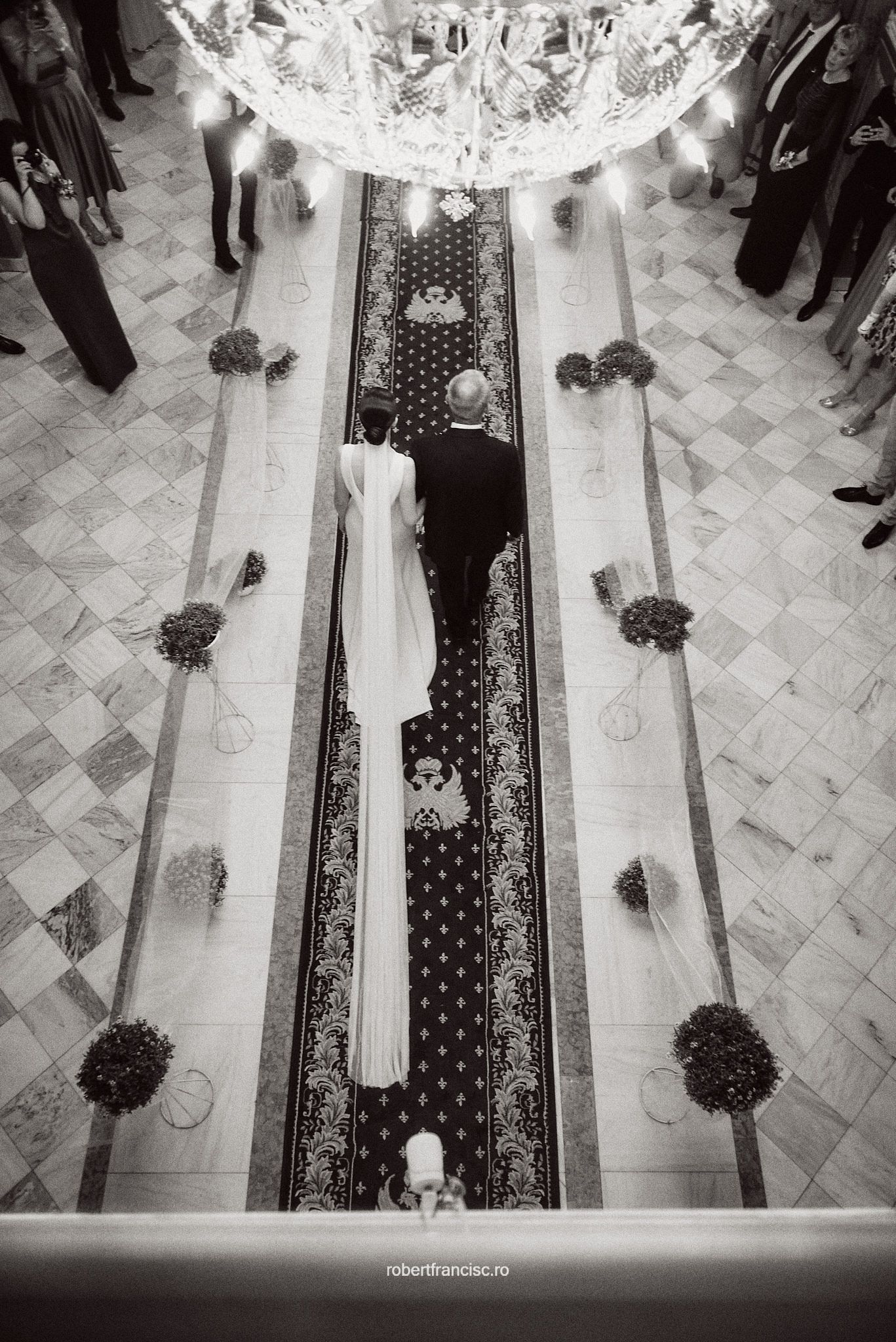 High angle black and white view of a decorated church aisle with an elegant carpet runner and floral arrangements.