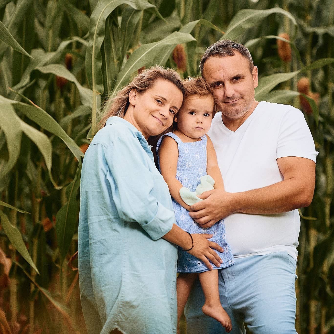 A family poses together in casual attire against tall corn stalks on a summer day.