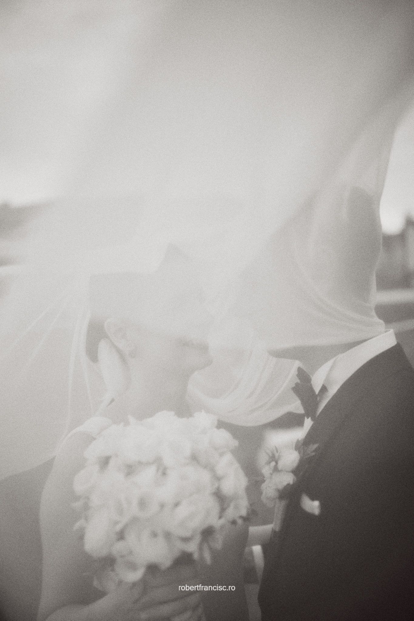 Artistic black and white wedding photo showing couple with veil and bouquet in soft dreamy focus.
