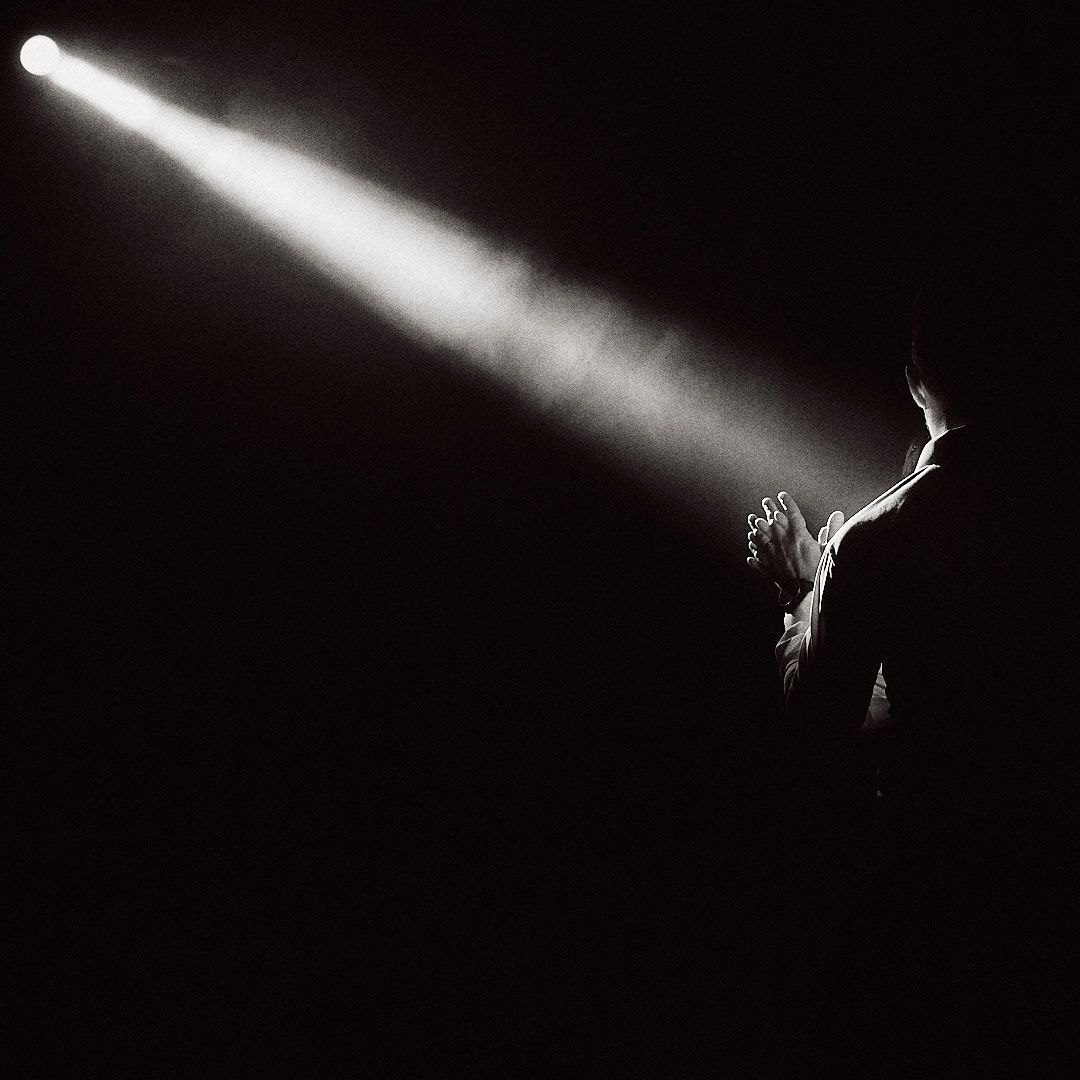 Dramatic black and white stage performance photo with single spotlight beam.