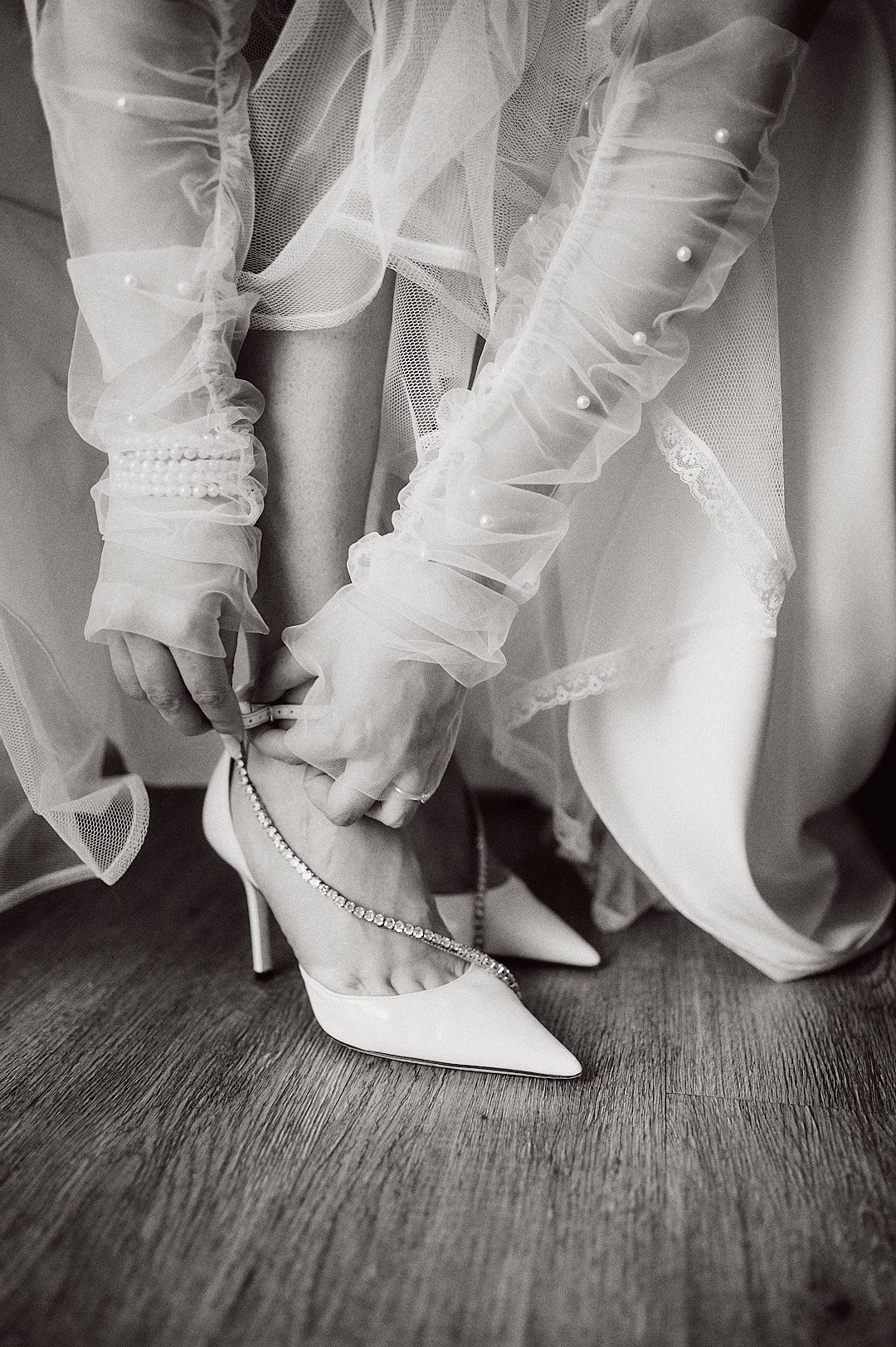 Detail shot of bride putting on white pointed heels with sheer gloves.