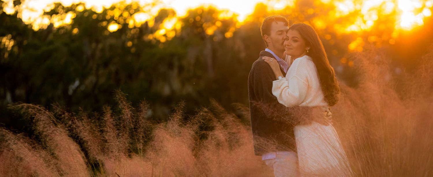 Couple embracing in golden sunset light among tall grass, romantic outdoor wedding photography.