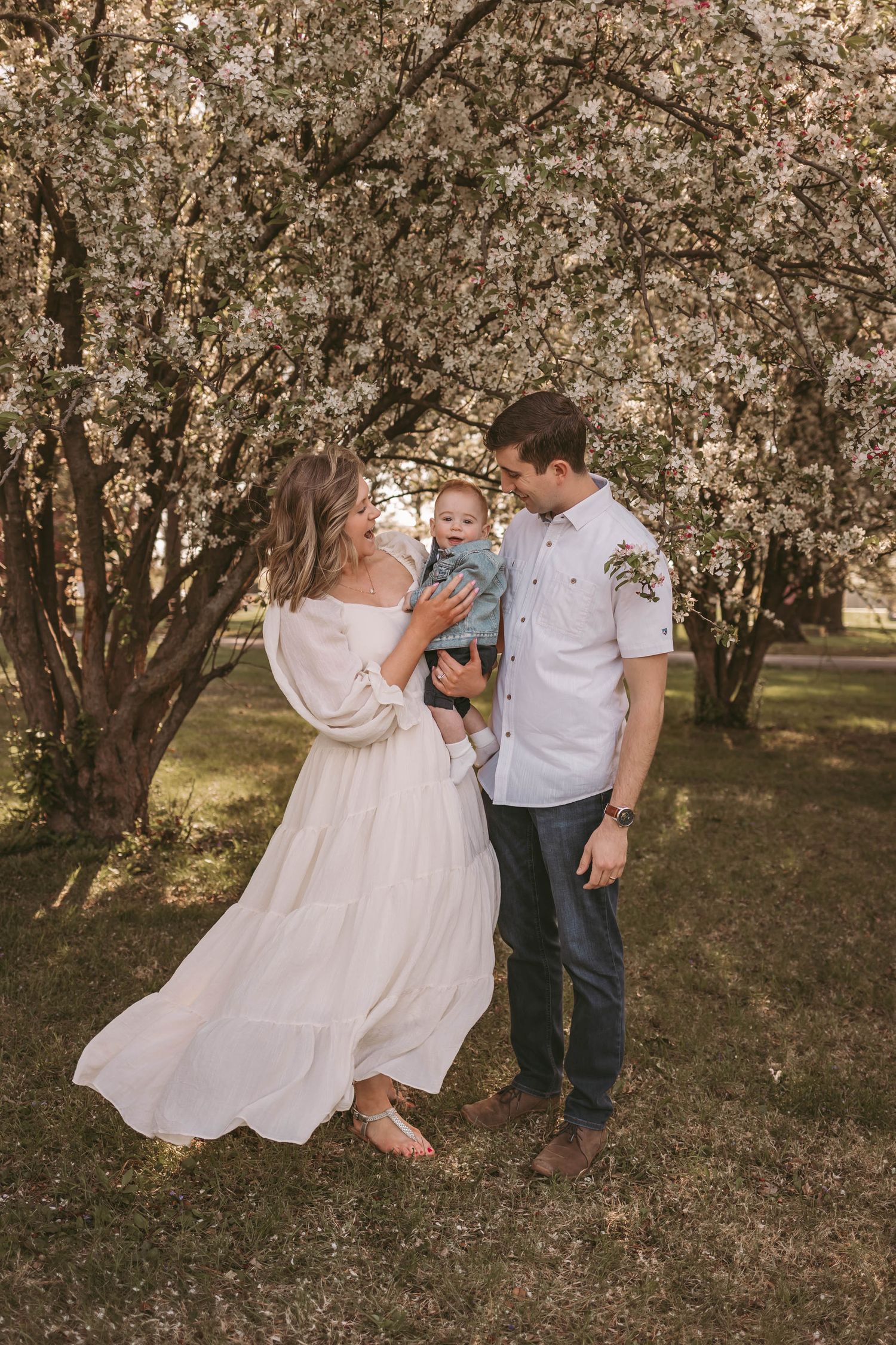 Mom and dad hold and look at their baby boy among the blossoms in a Des Moines area park during a lifestyle family photo session.