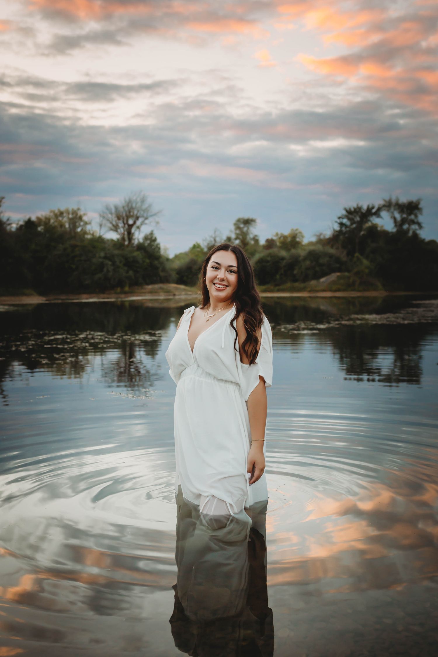 High school senior girl poses in a lake at sunset in a Des Moines area park during a lifestyle senior photo session.