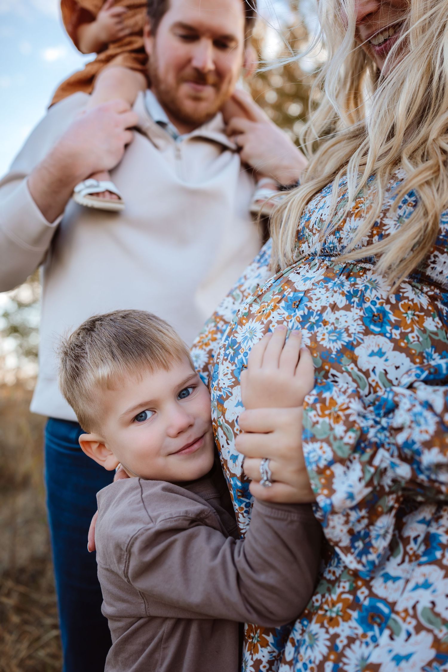 Little boy cradles mom's pregnant belly in a Des Moines area field at sunset during lifestyle maternity photo session.