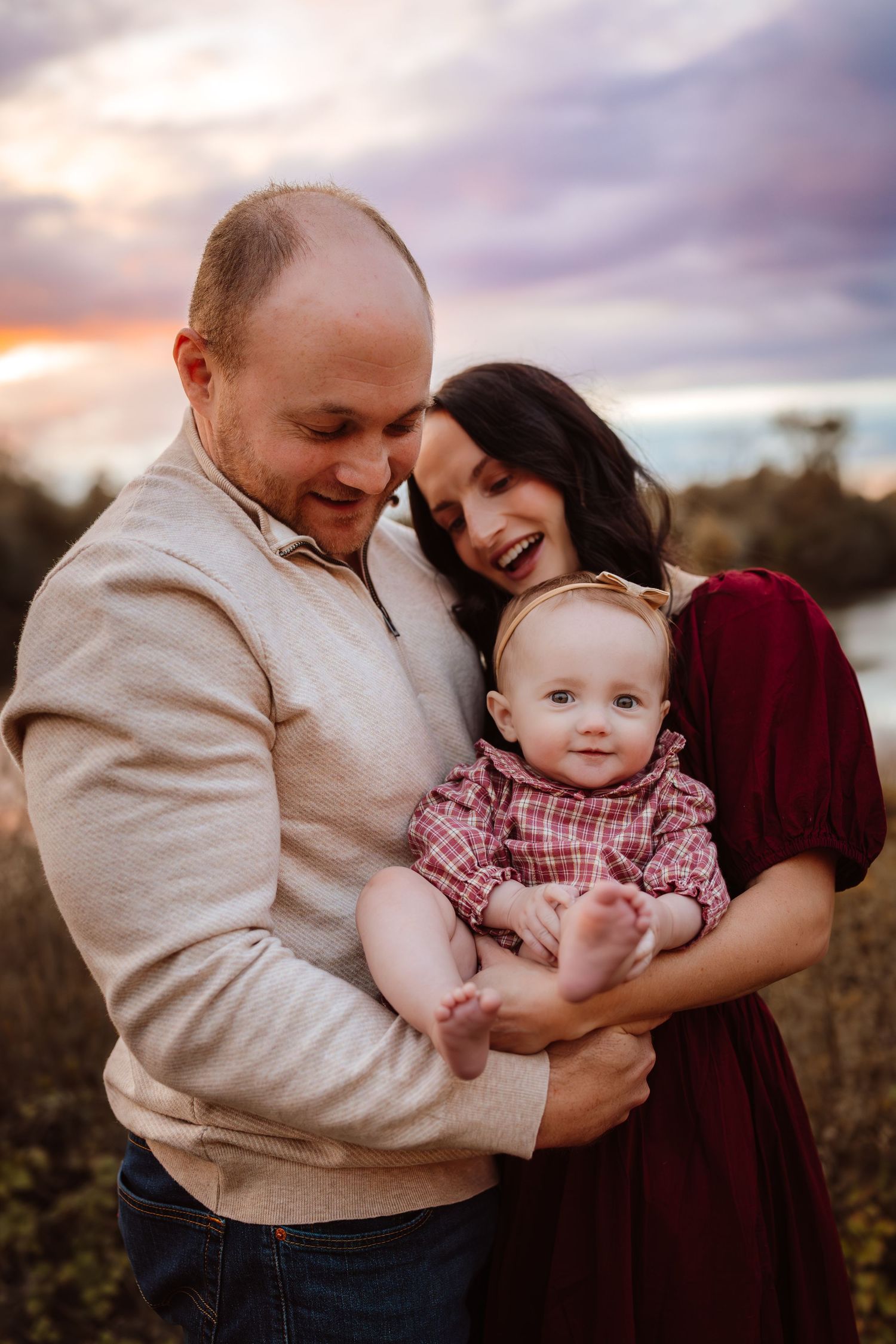 Parents hold baby girl as in a Des Moines area park at sunset during a lifestyle family photo session.