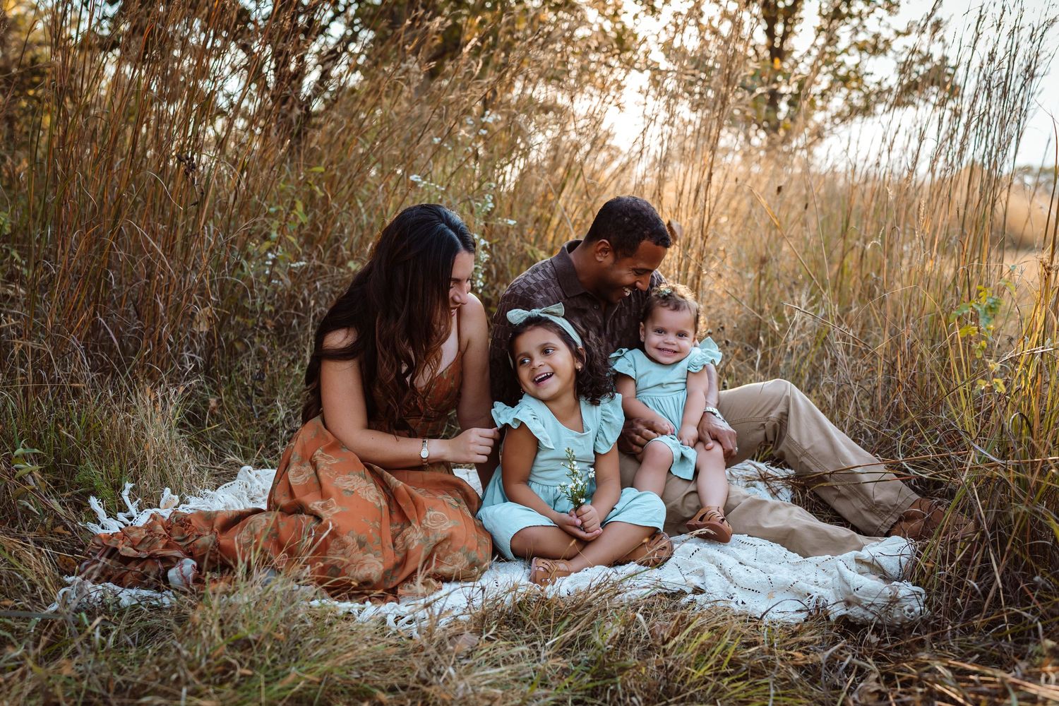 Family sits on vintage blanket in a Des Moines area park at sunset during a lifestyle family photo session.