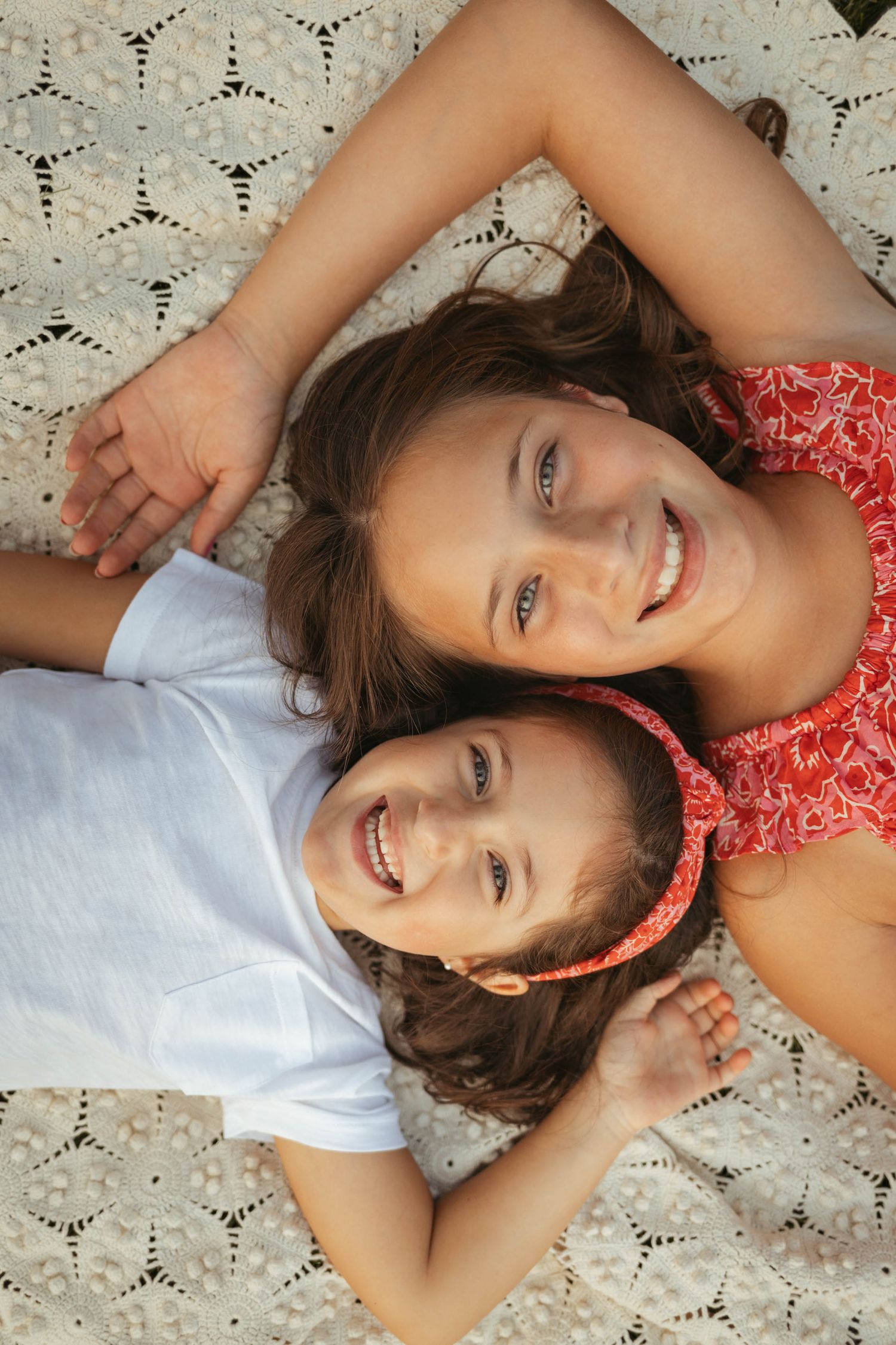 Sisters lay with their heads together in a Des Moines area park during a lifestyle family child milestone photo session.