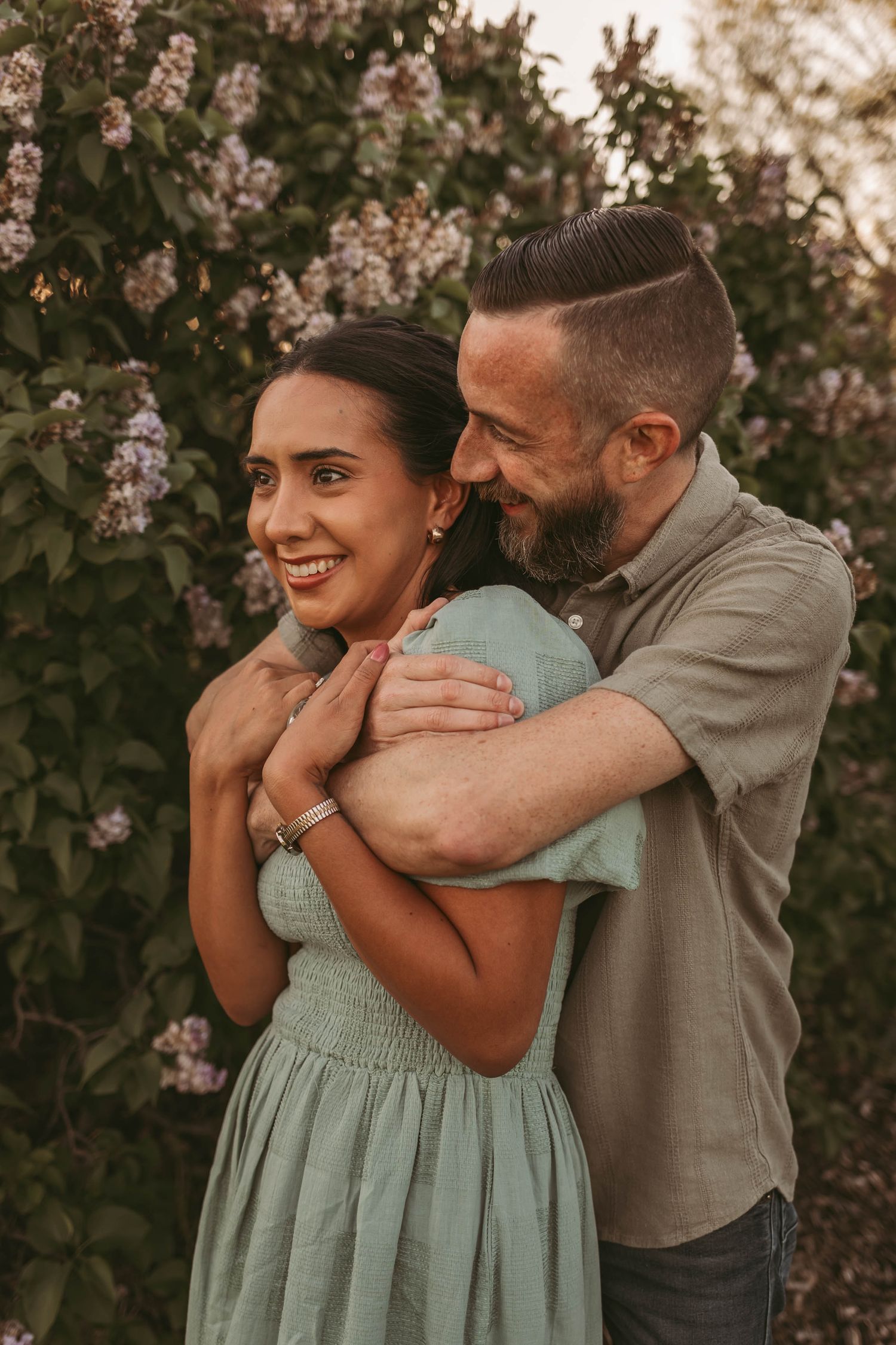 Couple embracing in front of a lilac bush in a Des Moines area park during a lifestyle family photo session.