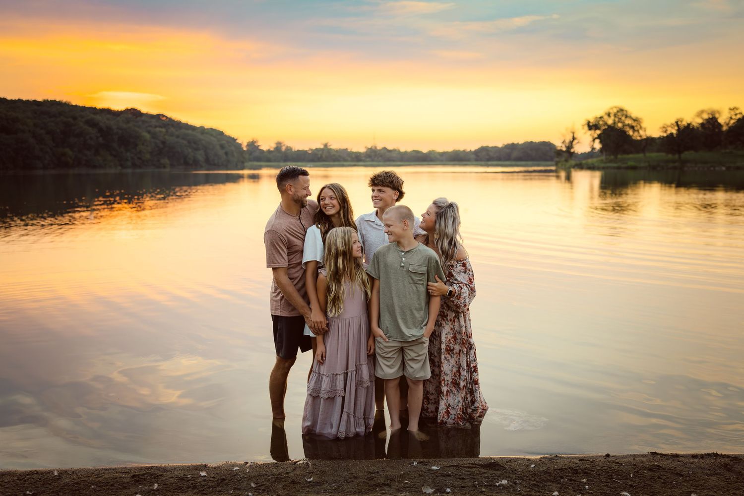 Family embraces in a lake in a Des Moines area park at sunset during a lifestyle family photo session.