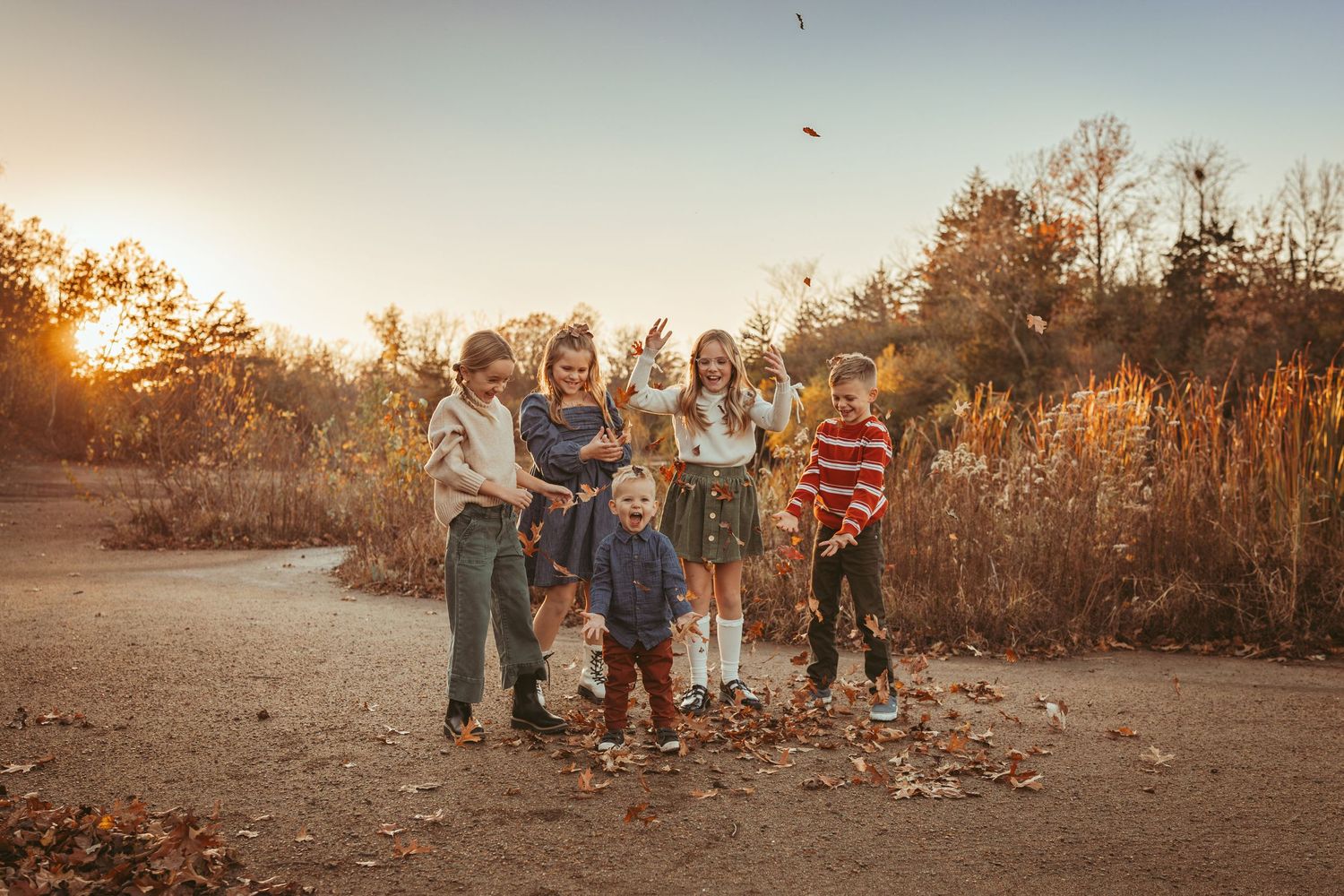Children throw leaves into the air a Des Moines area park at sunset during a lifestyle family photo session.