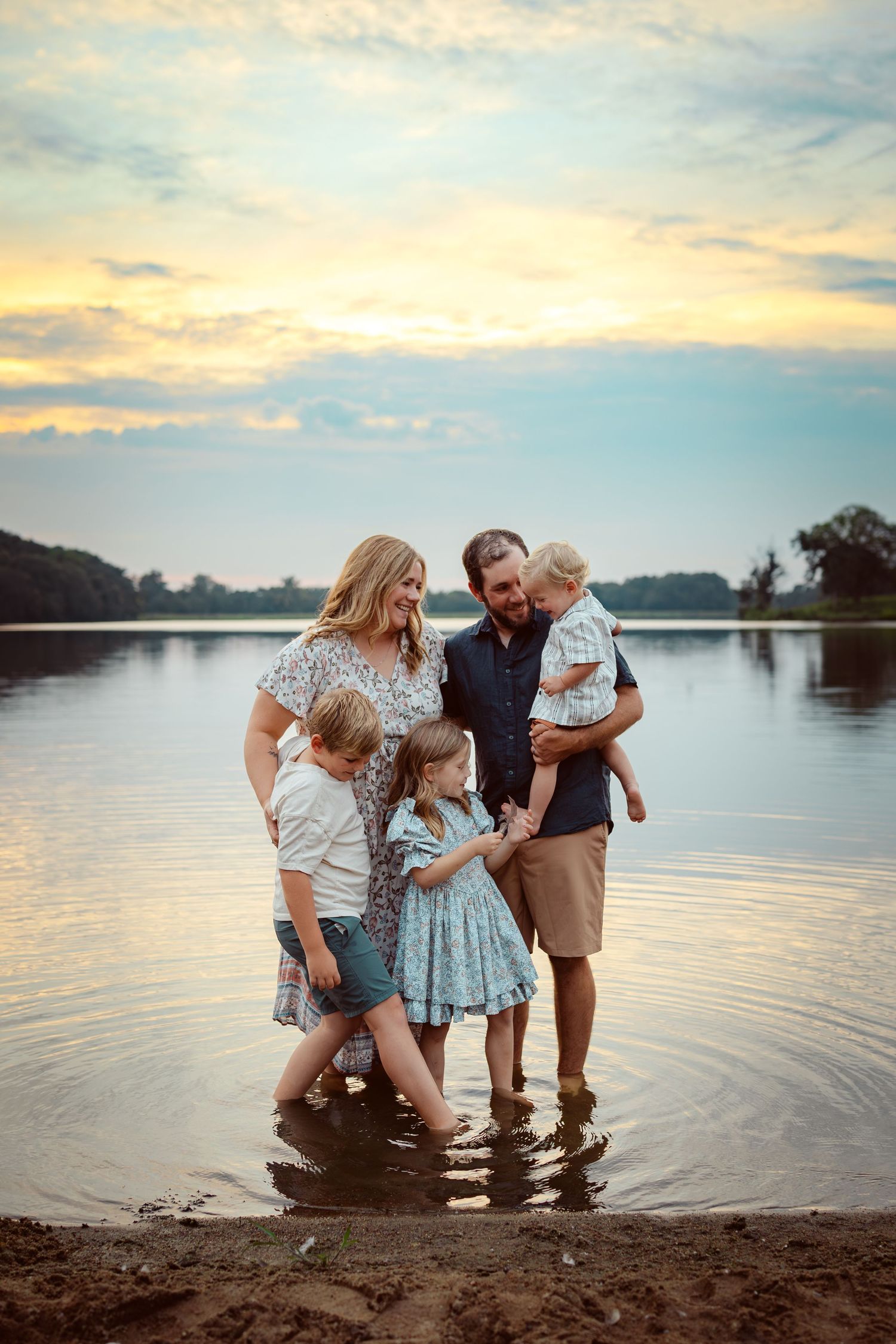 Family embraces in a lake in a Des Moines area park at sunset during a lifestyle family photo session.
