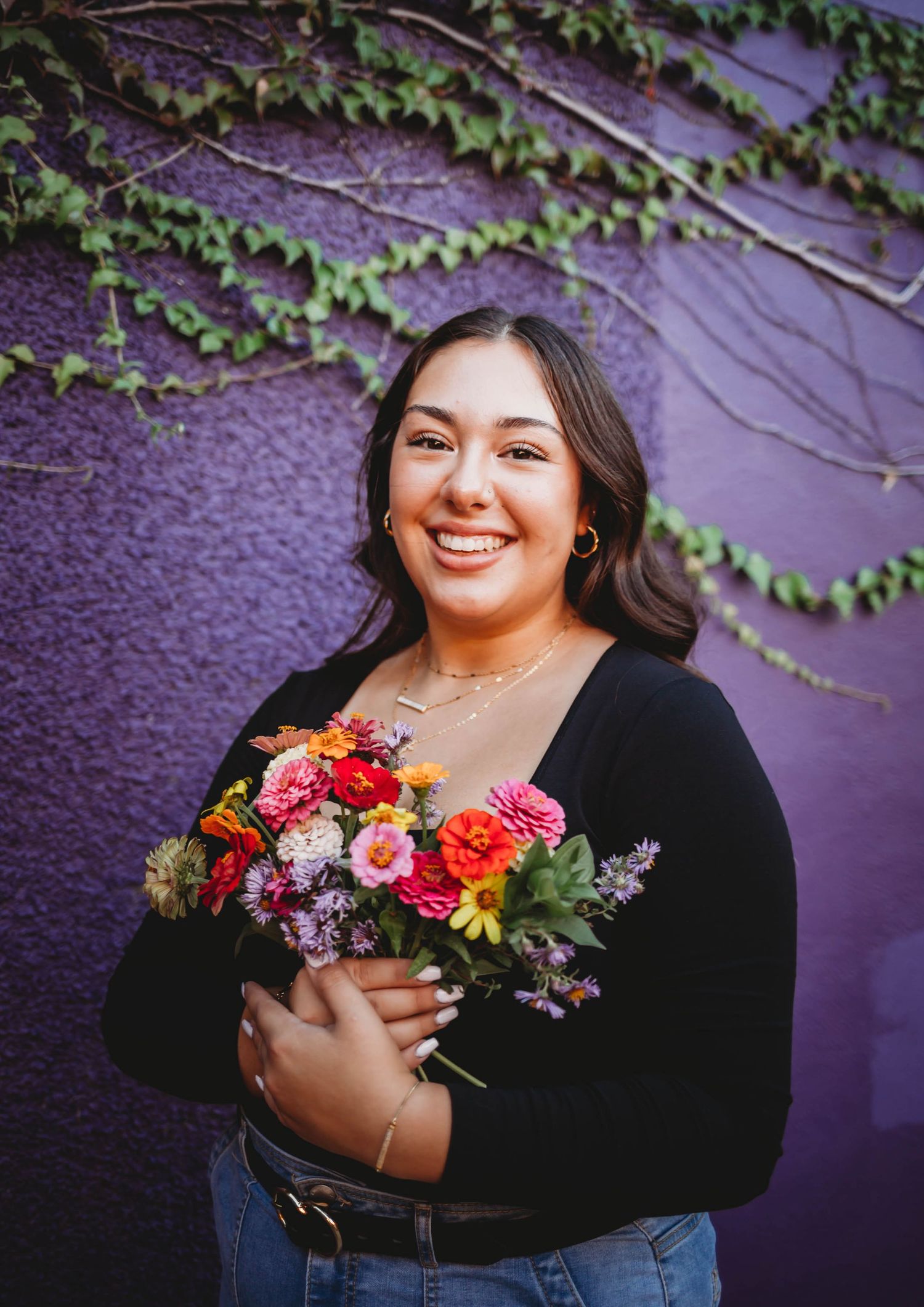 High school senior girl holds colorful flowers in front of a modern building in a Des Moines during a lifestyle senior photo session.