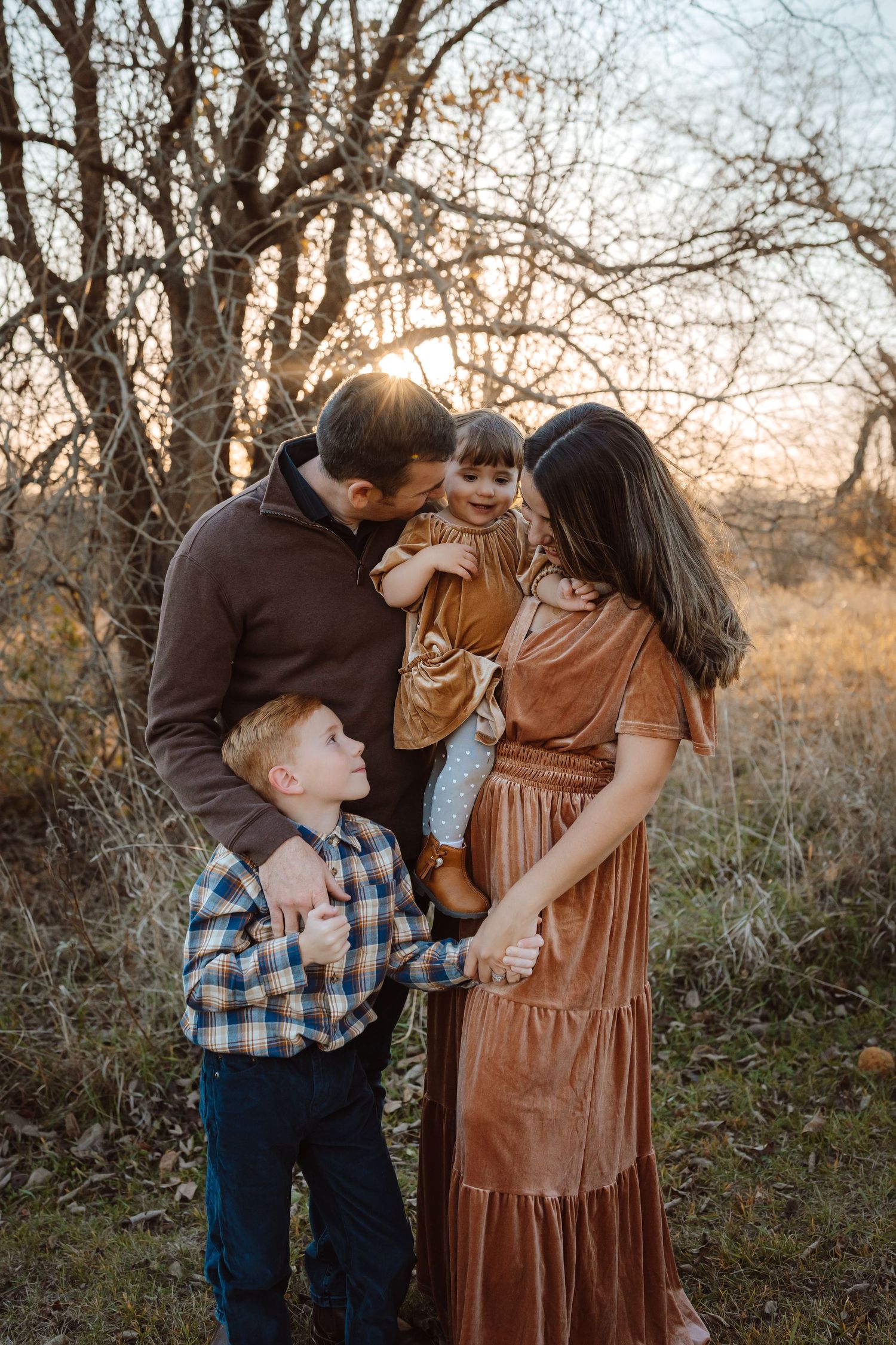 Family embraces in the golden light in a Des Moines area park at sunset during a lifestyle family photo session.