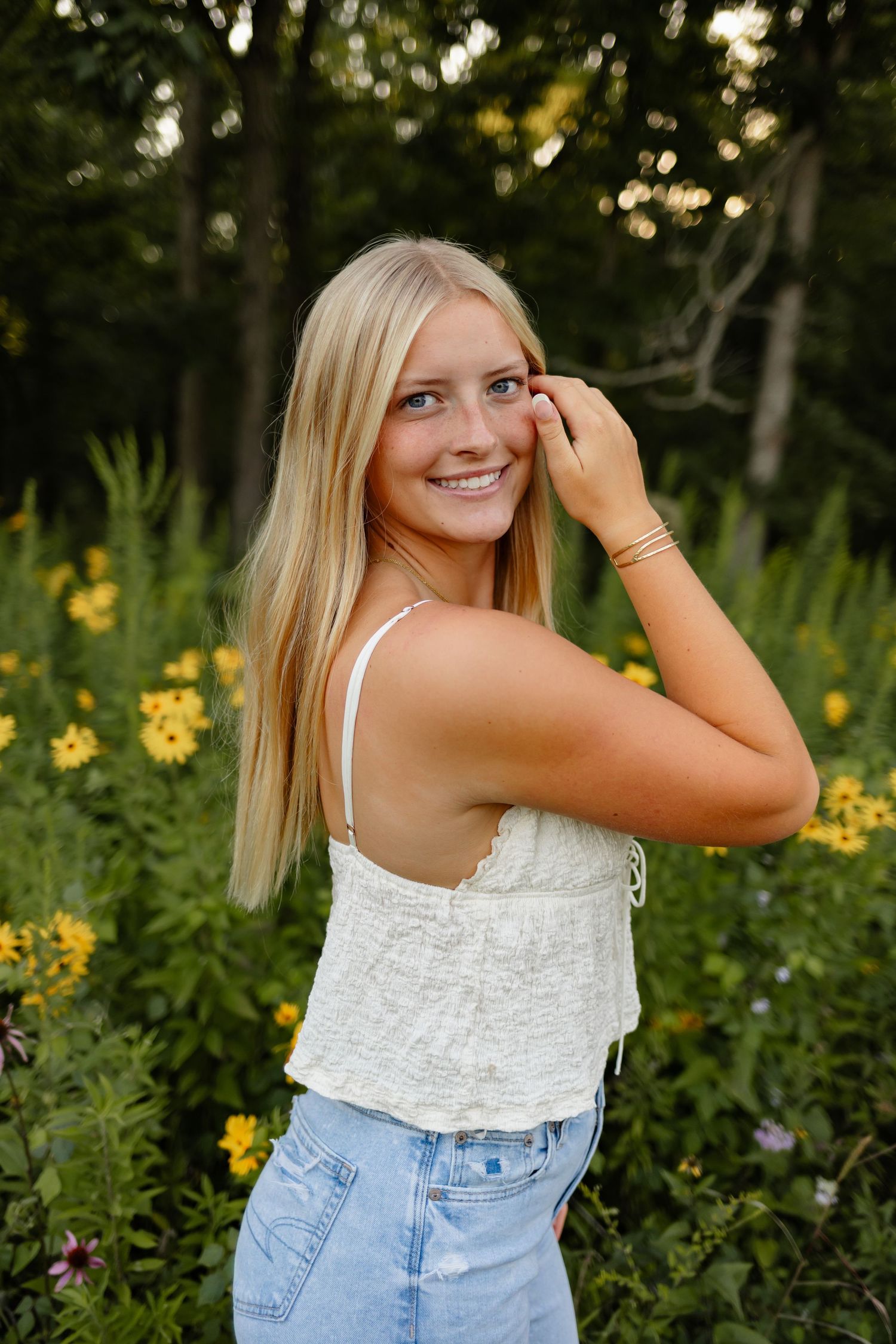 High school senior girl poses in a field of flowers in a Des Moines area park during a lifestyle senior photo session.