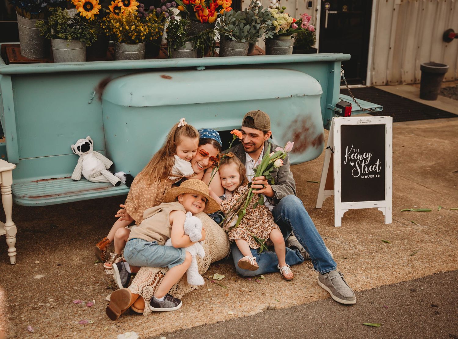 Family embraces while sitting in front of a flower cart in the Des Moines area during a lifestyle family photo session.