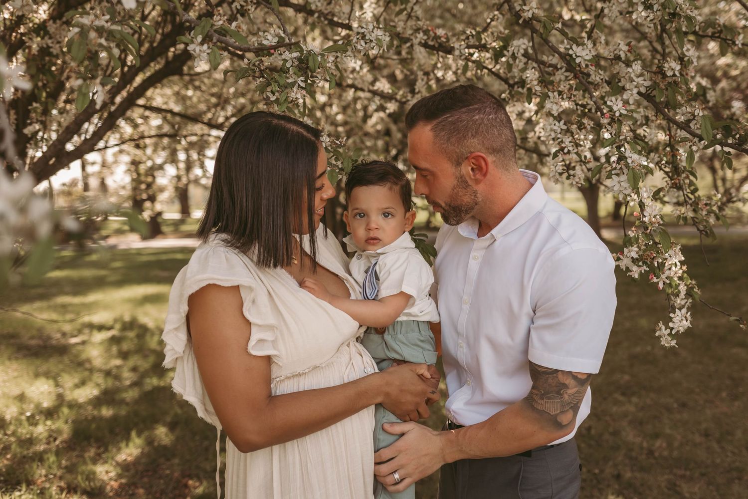 Mom and dad hold and look at their baby boy among the blossoms in a Des Moines area park during a lifestyle family photo session.