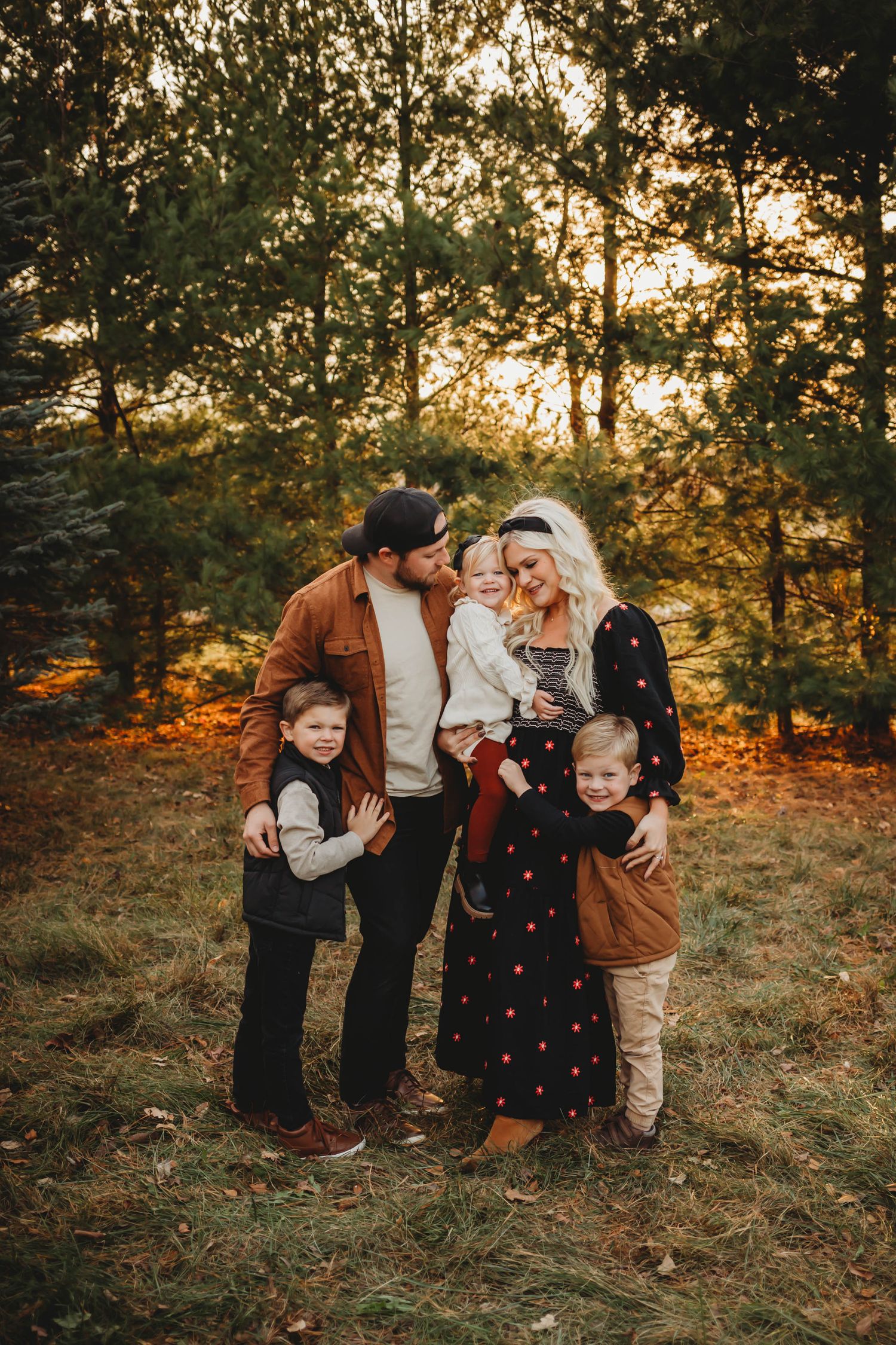 Family embraces in a Des Moines area evergreen field at sunset during a lifestyle family photo session.