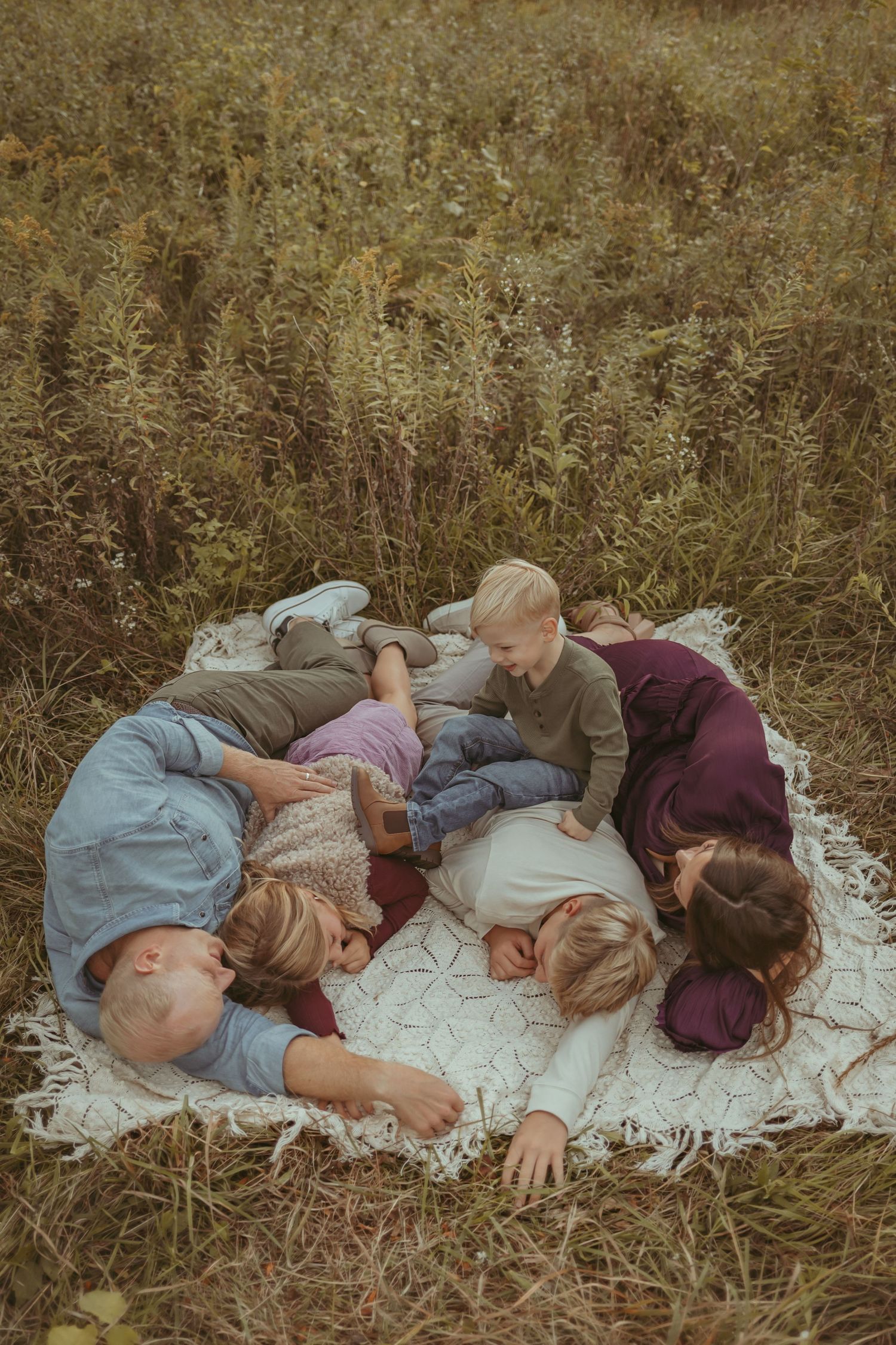 Family snuggles and lays together on a vintage blanket in a Des Moines area park during a lifestyle family photo session.