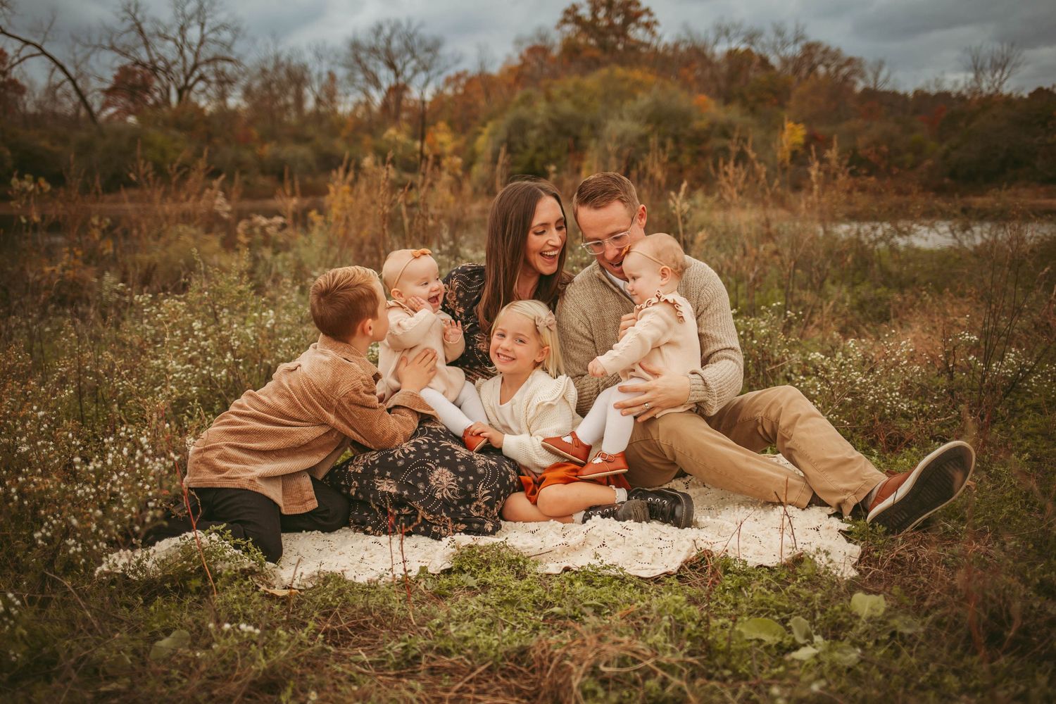 Family sits on a vintage blanket in a Des Moines area park at sunset during a lifestyle family photo session.