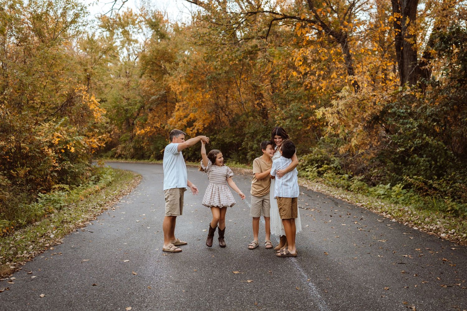 Dad twirls daughter as others look on in a Des Moines area park at sunset during a lifestyle family photo session.