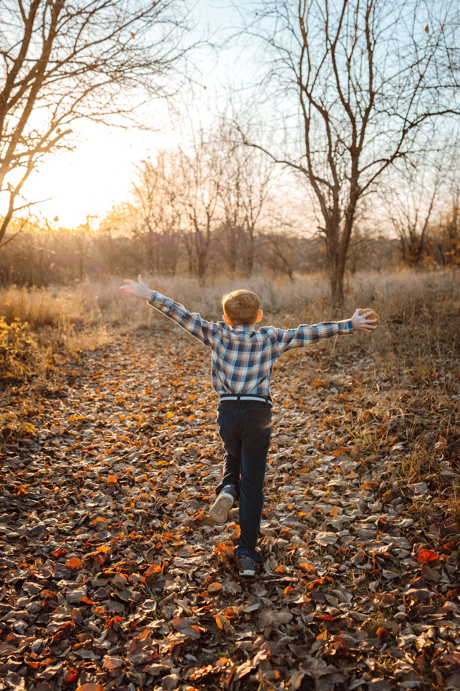 Young boy runs in leaves in a Des Moines area park during a lifestyle family child milestone photo session.