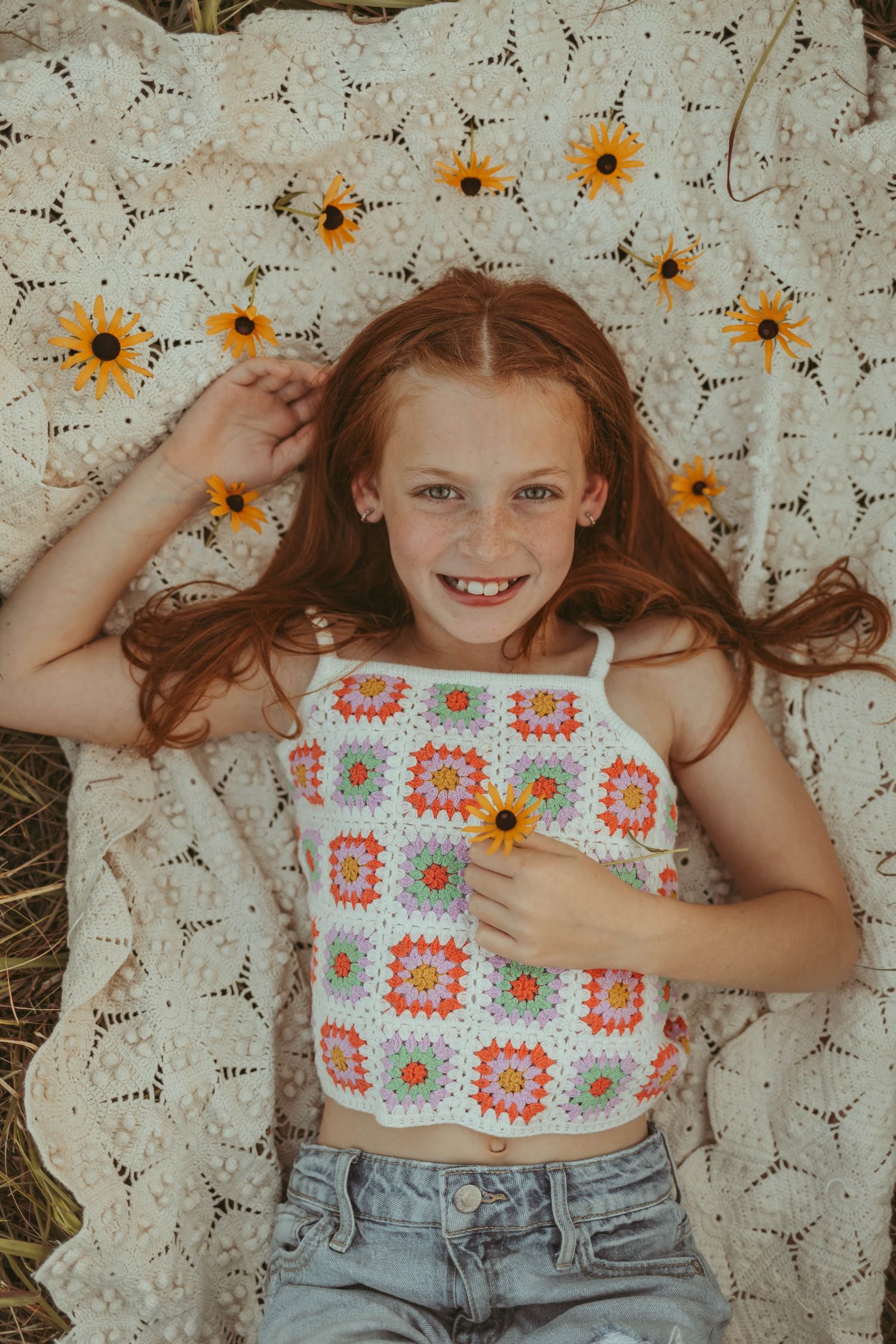 Young girl lays among flowers in a Des Moines area park at sunset during a lifestyle family child milestone photo session.