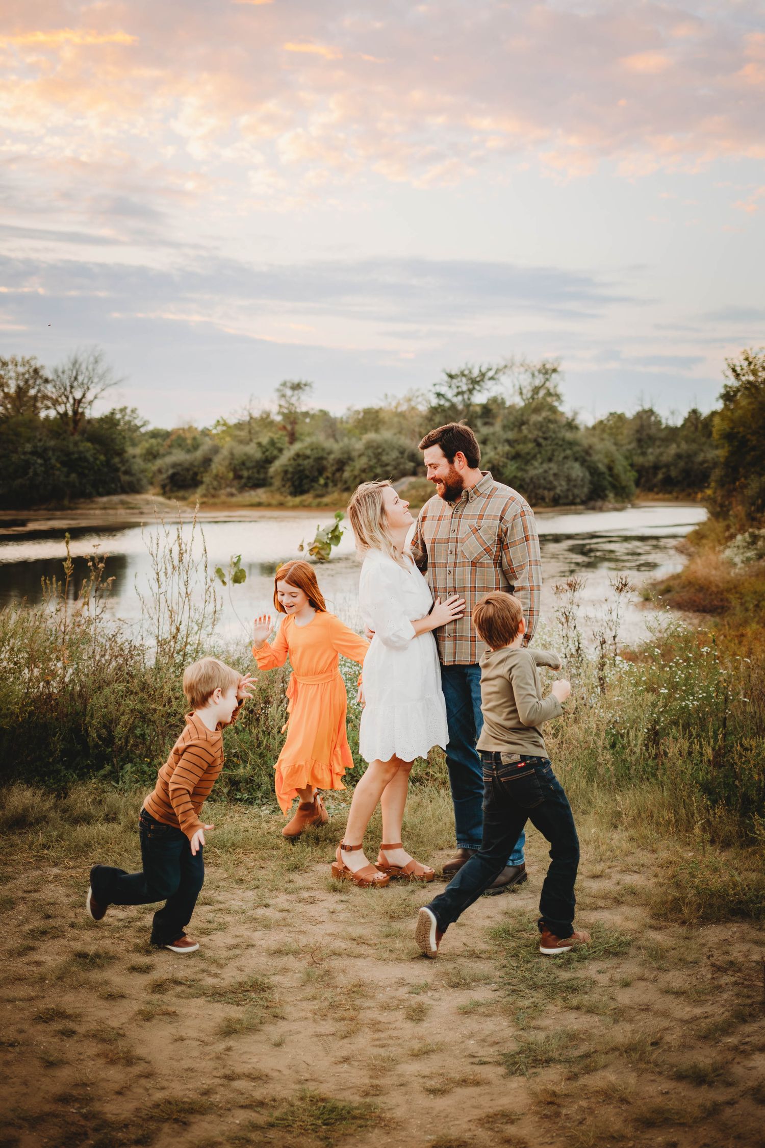 Children run around their mom and dad in front of a lake in a Des Moines area park during a lifestyle family session.