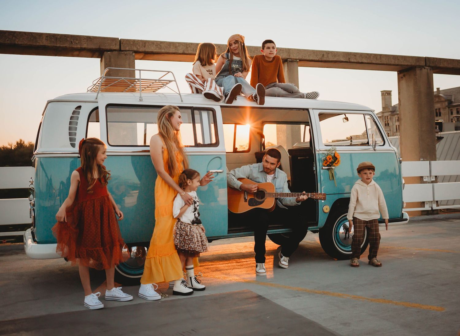 Family in and around a vintage van in a Des Moines area parking ramp at sunset during lifestyle family photo session.