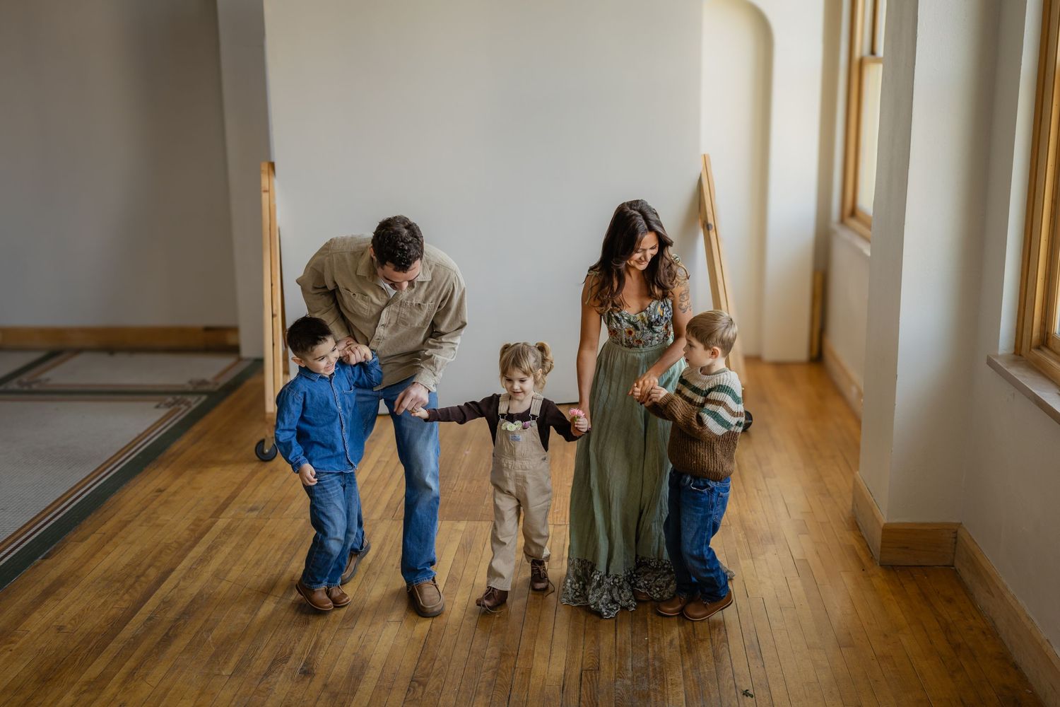 Family hold hands and walks in a Des Moines area studio during lifestyle family photo session.