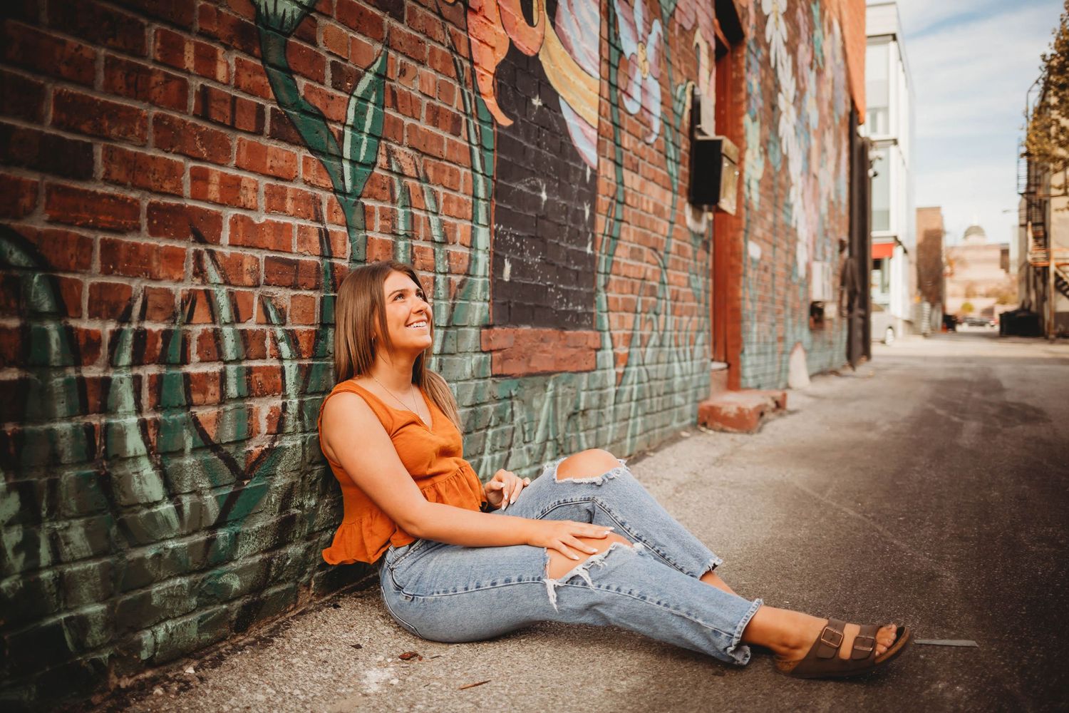 High school senior girl poses in front of a mural on a building in a Des Moines during a lifestyle senior photo session.