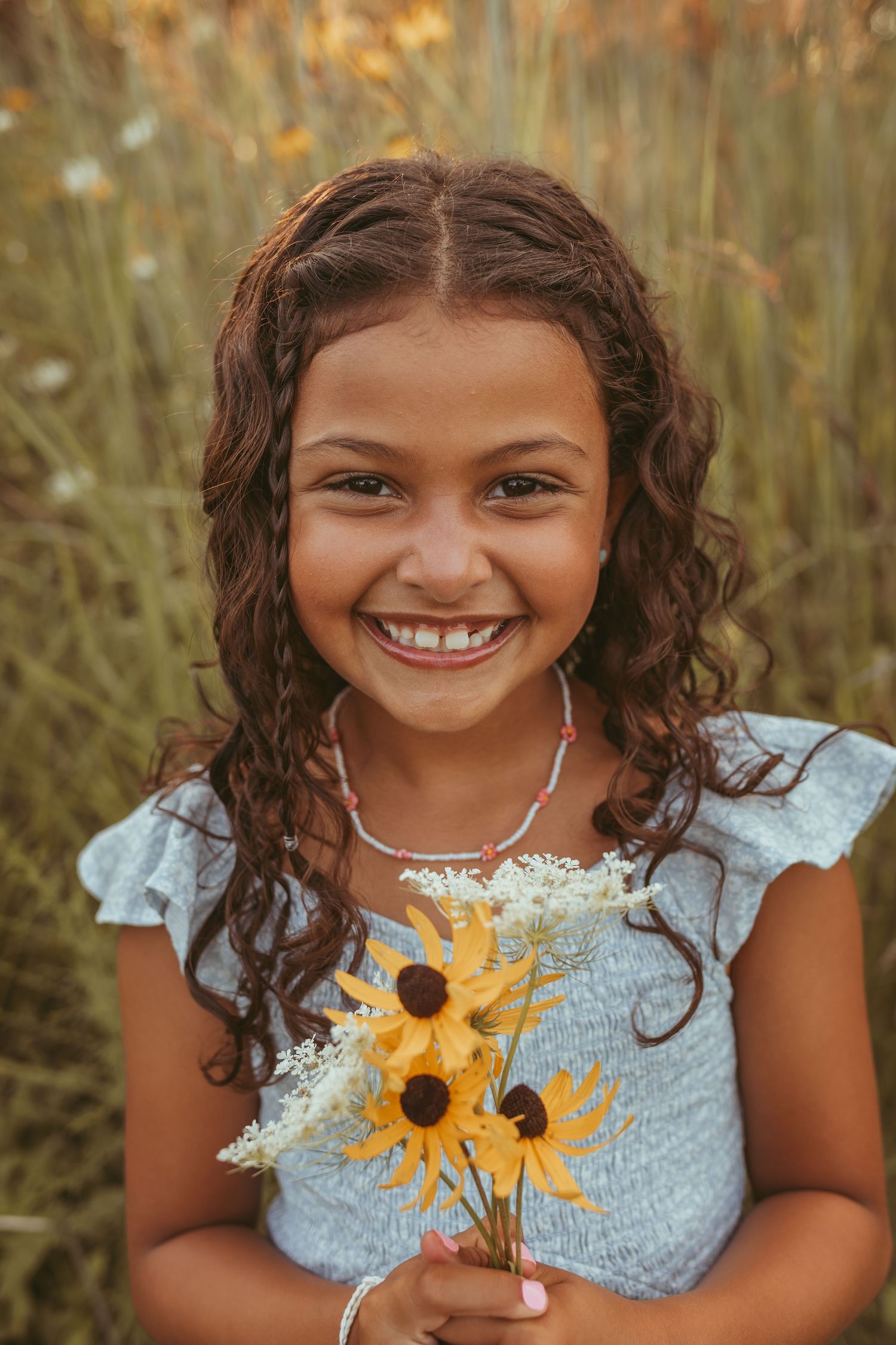 Young girl holds wildflowers in a Des Moines area park at sunset during a lifestyle family child milestone photo session.