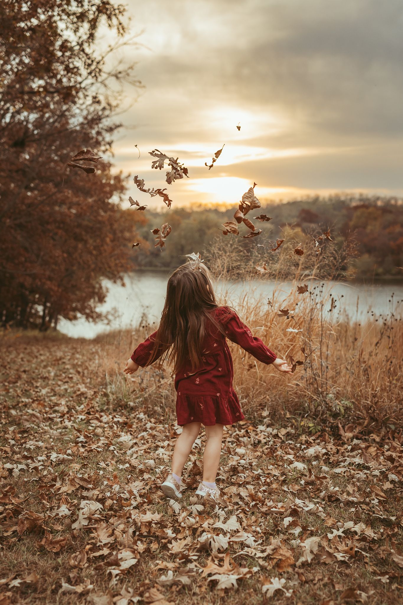 Young girl throws leaves in the air in a Des Moines area park at sunset during a lifestyle family child milestone photo session.