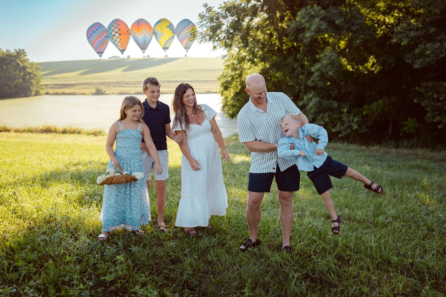 Family plays as before hot air balloons in a Des Moines area park at sunrise during a lifestyle family photo session.
