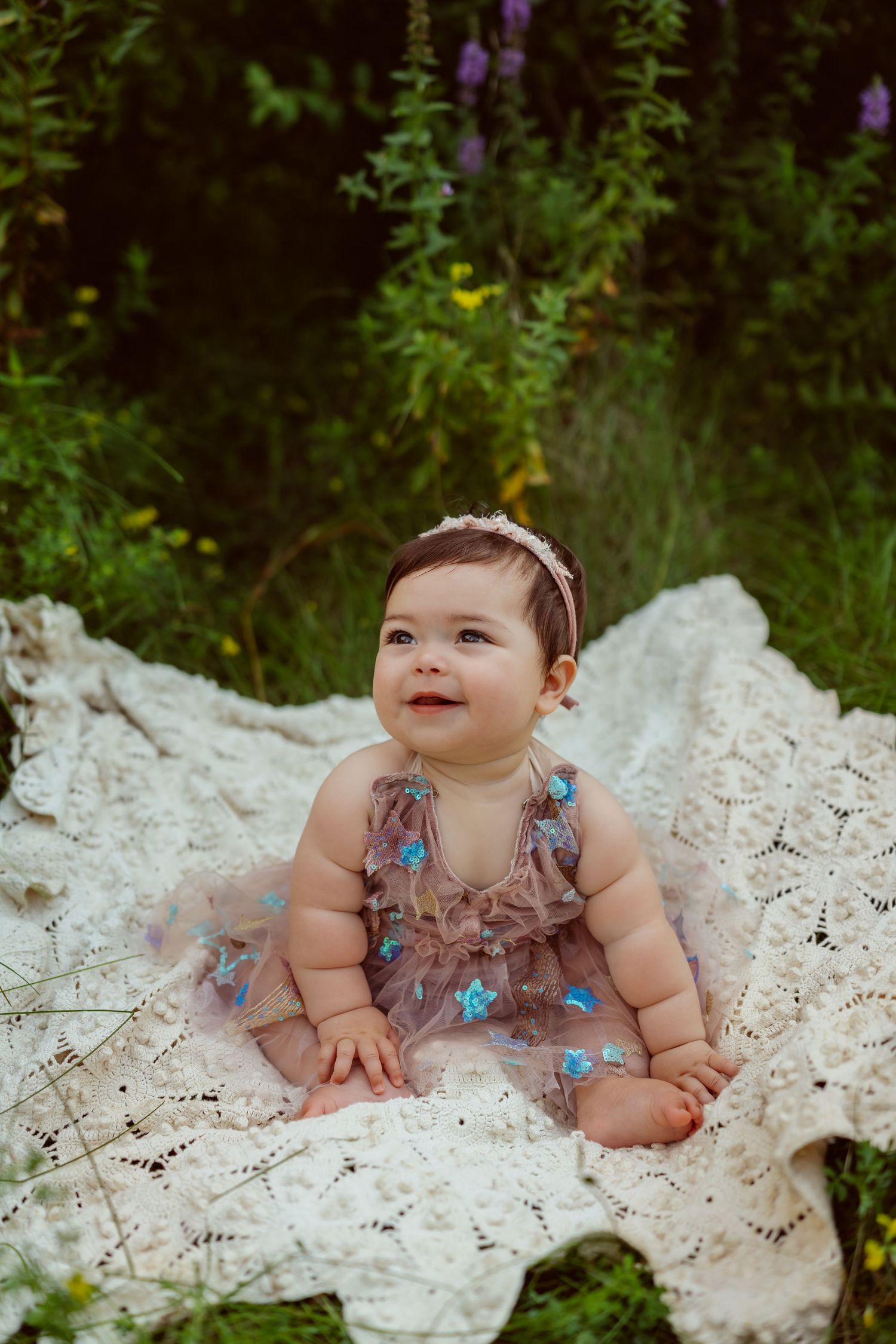 Baby girl sits on a vintage blanket in a Des Moines area park during a lifestyle family child milestone photo session.
